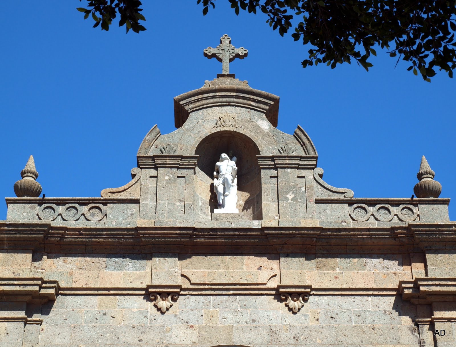 A colonial-era chapel in Aguimes Old Town features ornate stonework and a religious statue sheltered beneath a decorative arch.
