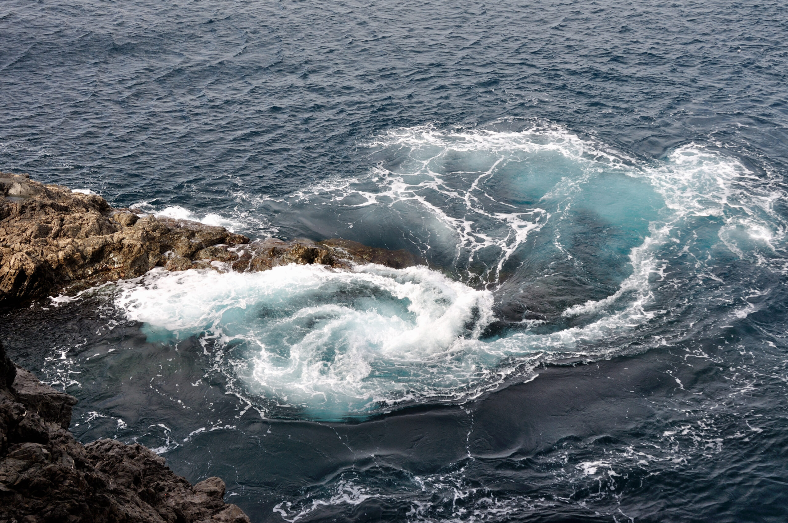 Powerful Atlantic waves crash against the rocky shore near Ajuy, creating striking patterns of turquoise water and white sea foam.