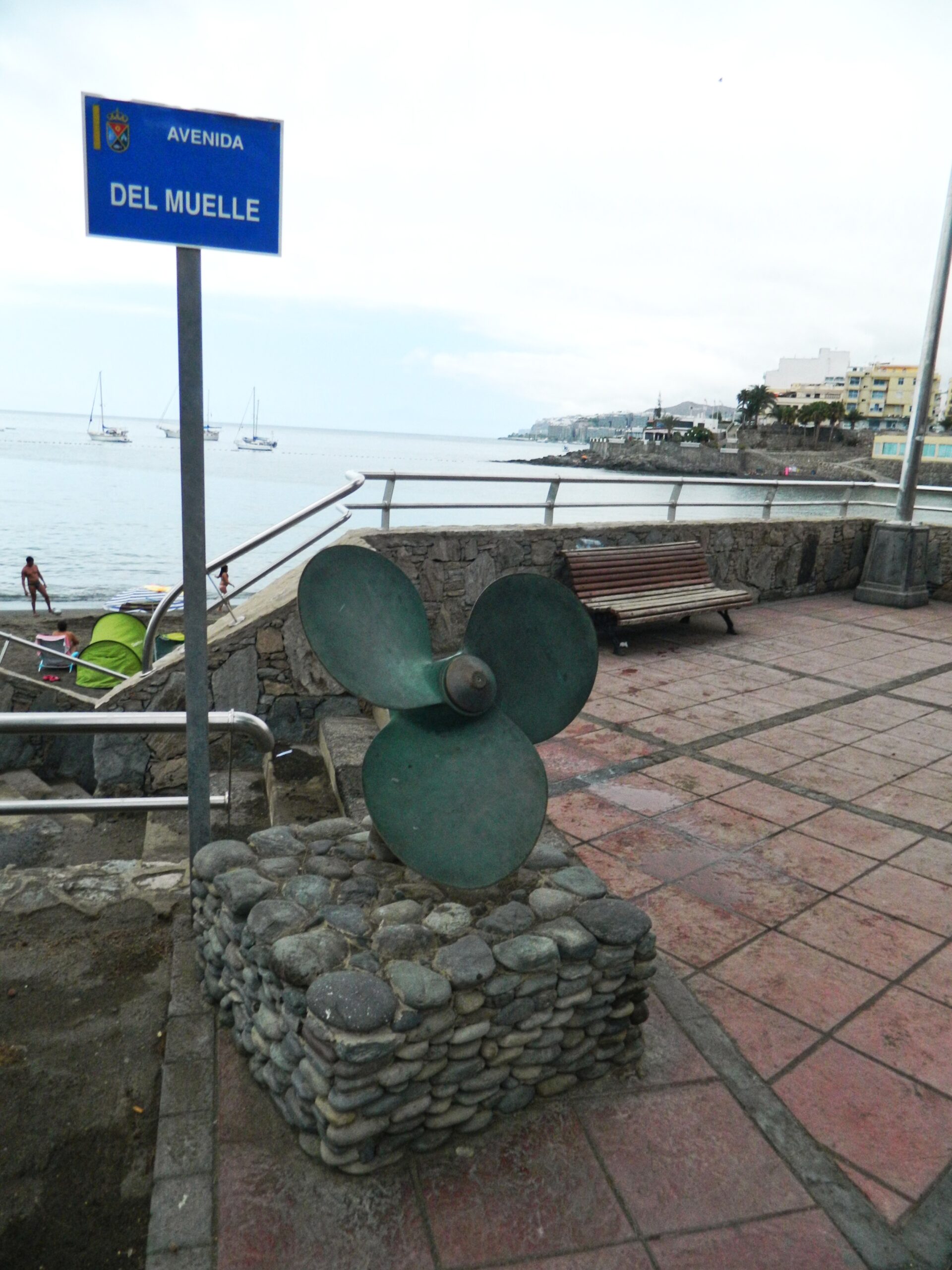 Avenida del Muelle and its waterfront sculpture overlook Arguineguín’s working harbour and coastal promenade.