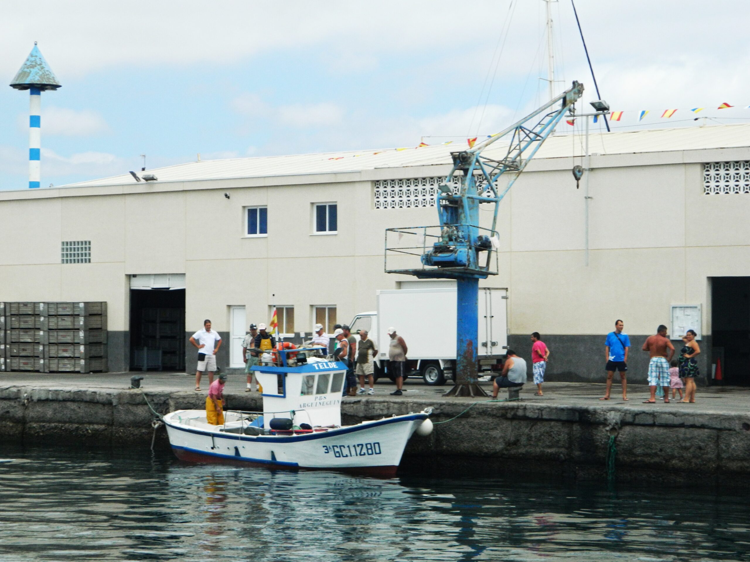 Arguineguín Harbor features traditional fishing boats and port infrastructure, with the blue‑and‑white lighthouse marking the waterfront.