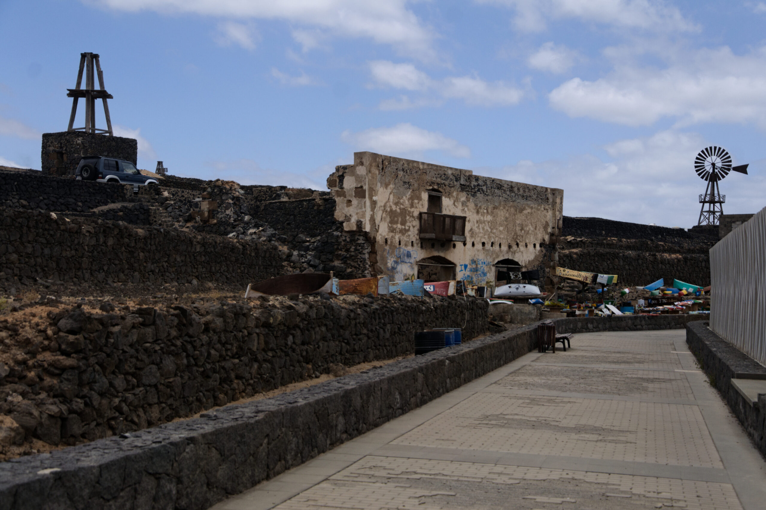 The historic marina area features a restored waterfront walkway alongside a fortified building, traditional fishing equipment, and period structures reflecting the port's maritime heritage.