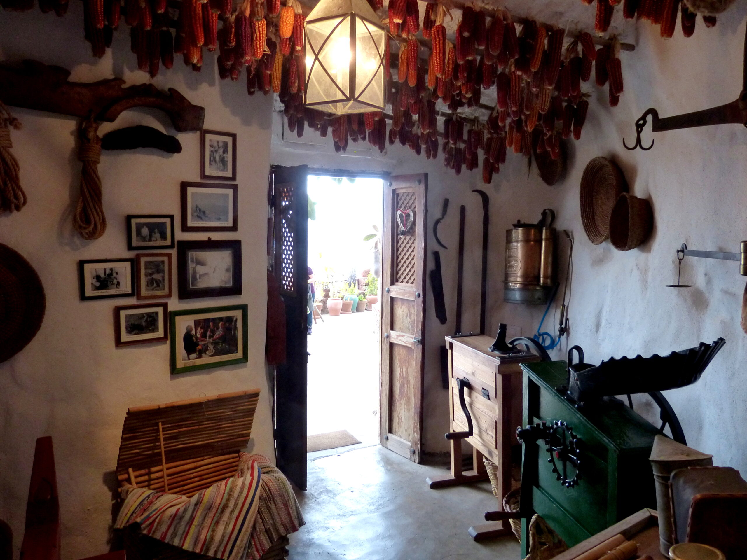 A traditional cave home interior displays local crafts, historical photographs, and hanging peppers characteristic of rural Canarian life.