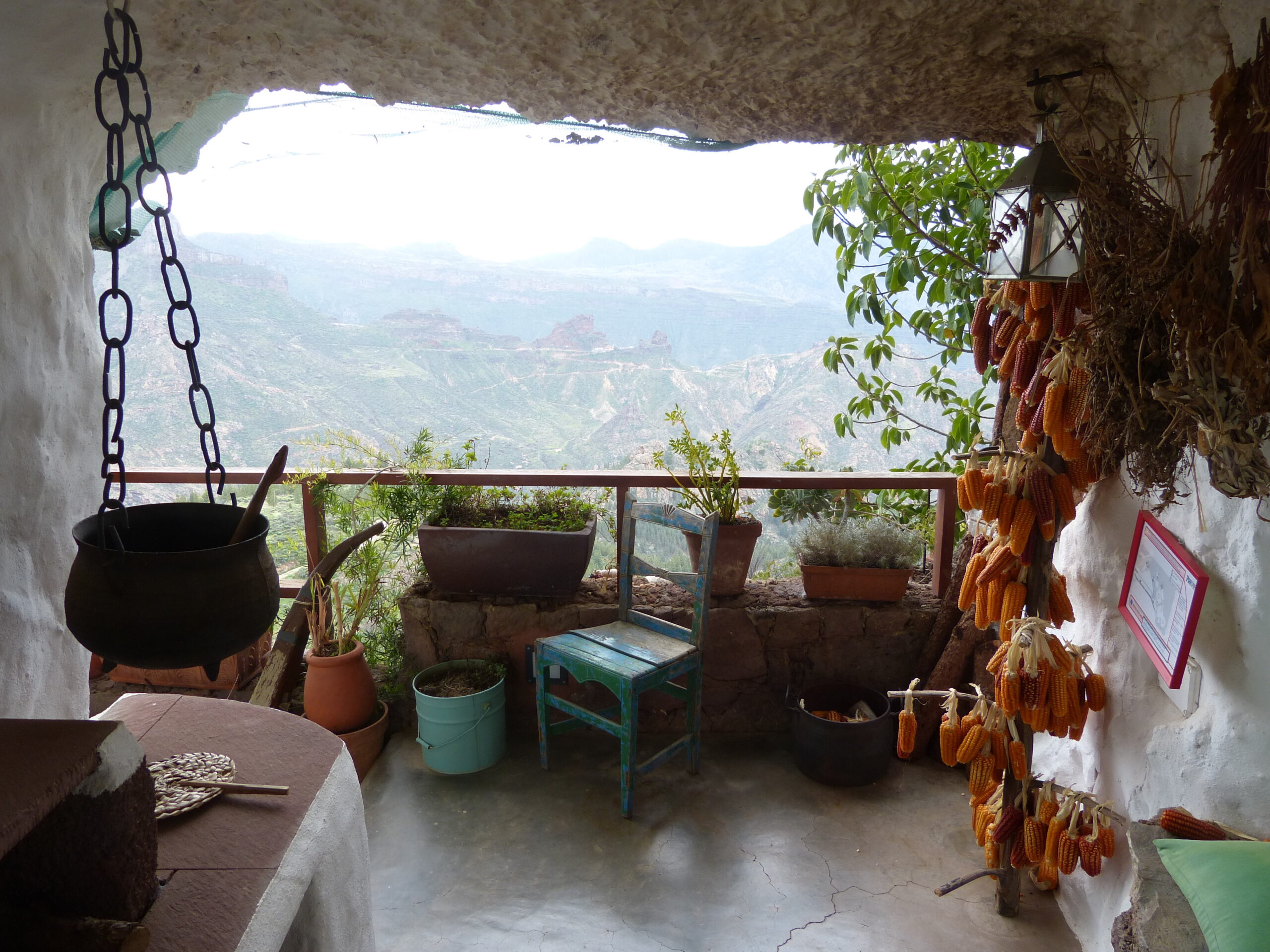 A traditional cave home in Artenara opens onto sweeping views of Gran Canaria's dramatic volcanic landscape, with everyday furnishings and dried peppers preserved in the cool interior.