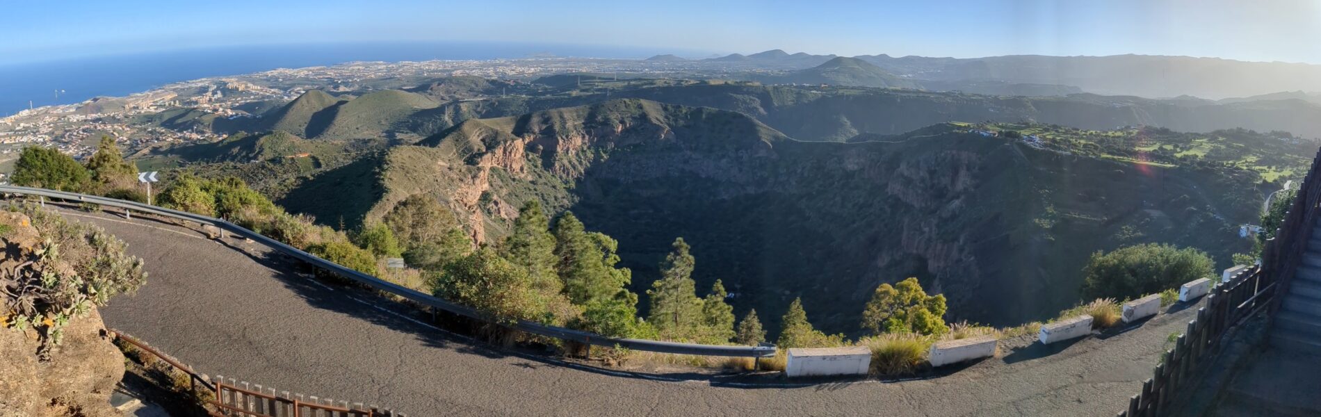 Aerial view of Bandama crater with steep volcanic walls, forested interior, and coastal plains visible in the distance under clear sky