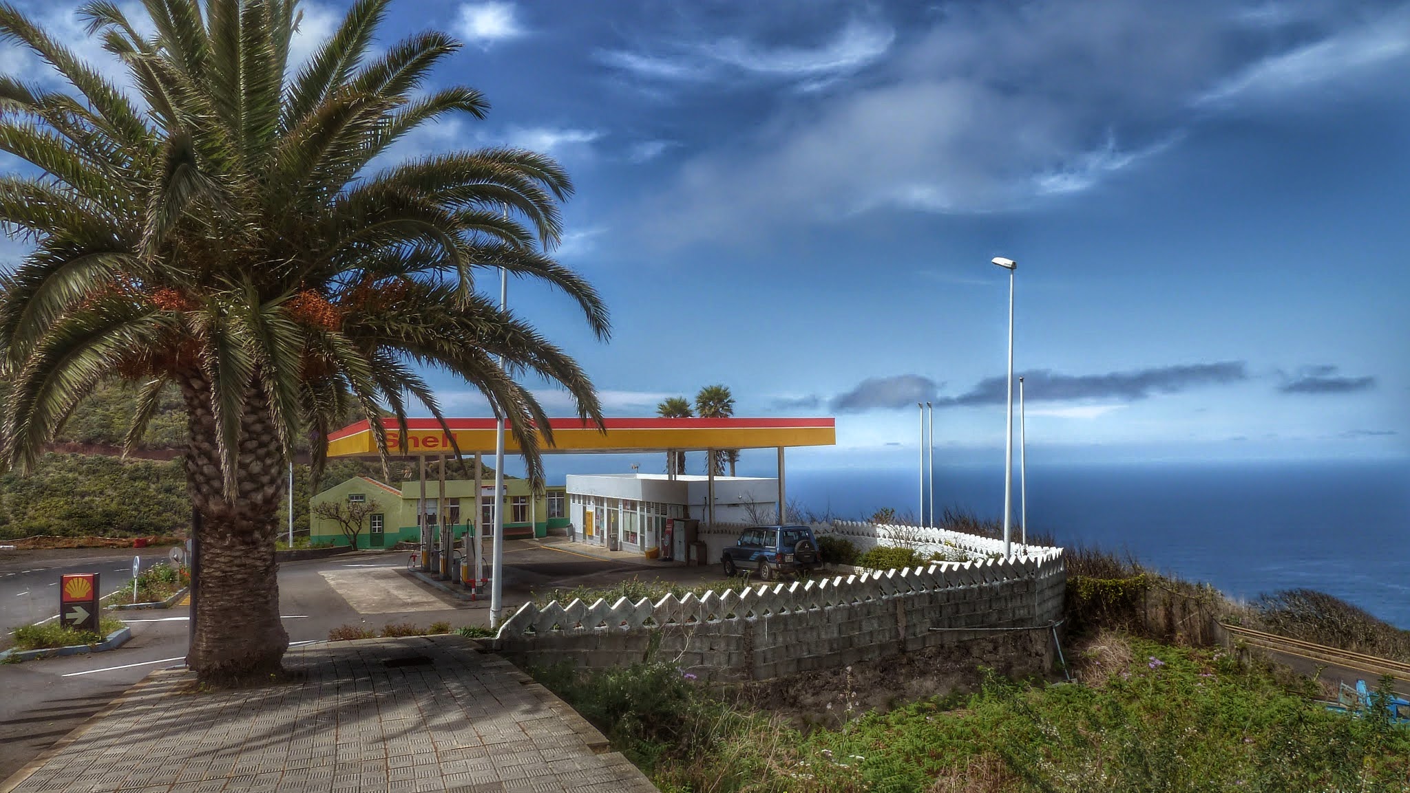 A roadside gas station sits perched on the windward coast of La Palma, with sweeping ocean views and native vegetation along the cliff edge.