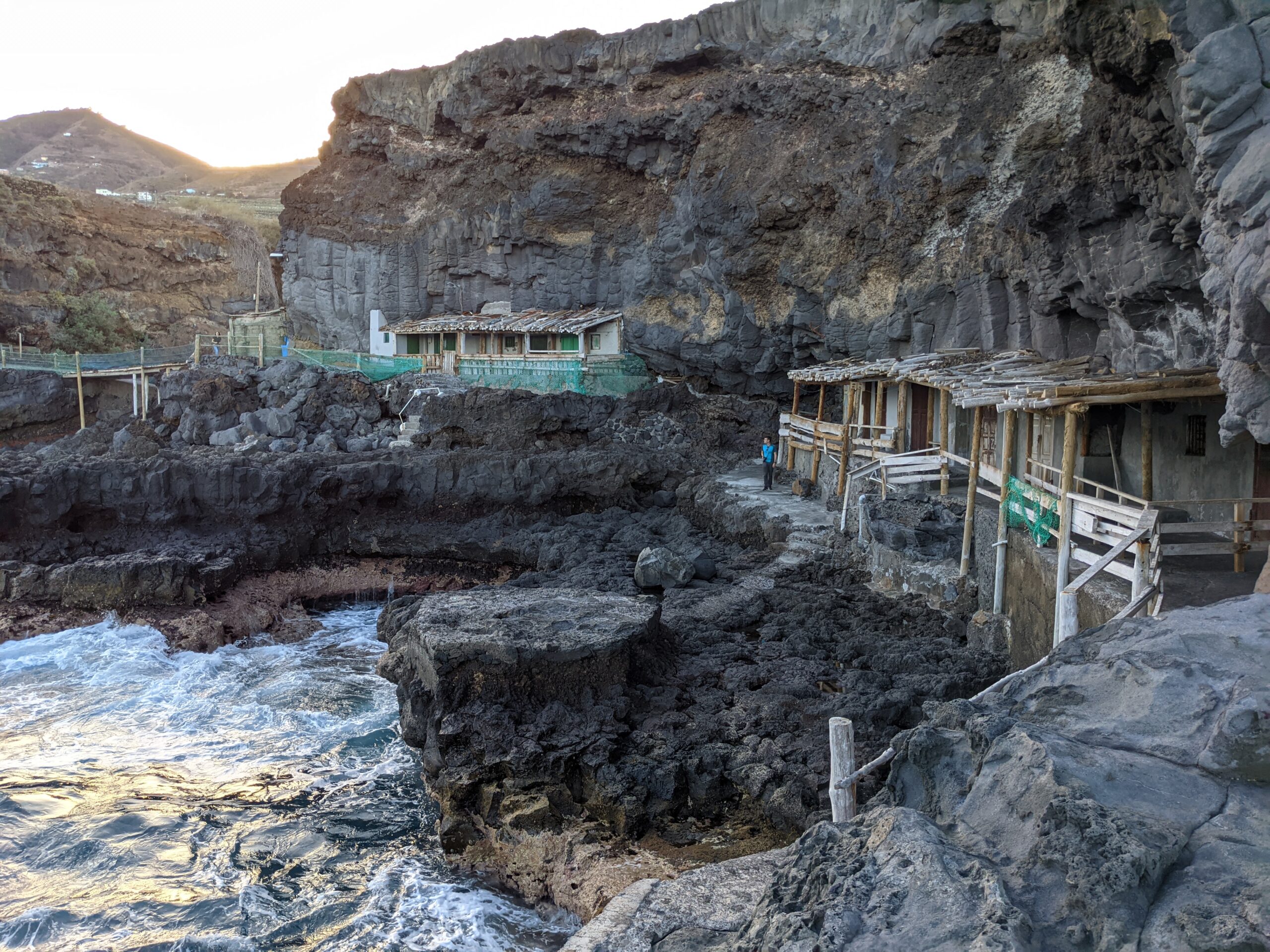 Traditional wooden fishing shelters nestle against the dramatic basalt cliffs of the Barlovento Coast, where the volcanic landscape meets the Atlantic.