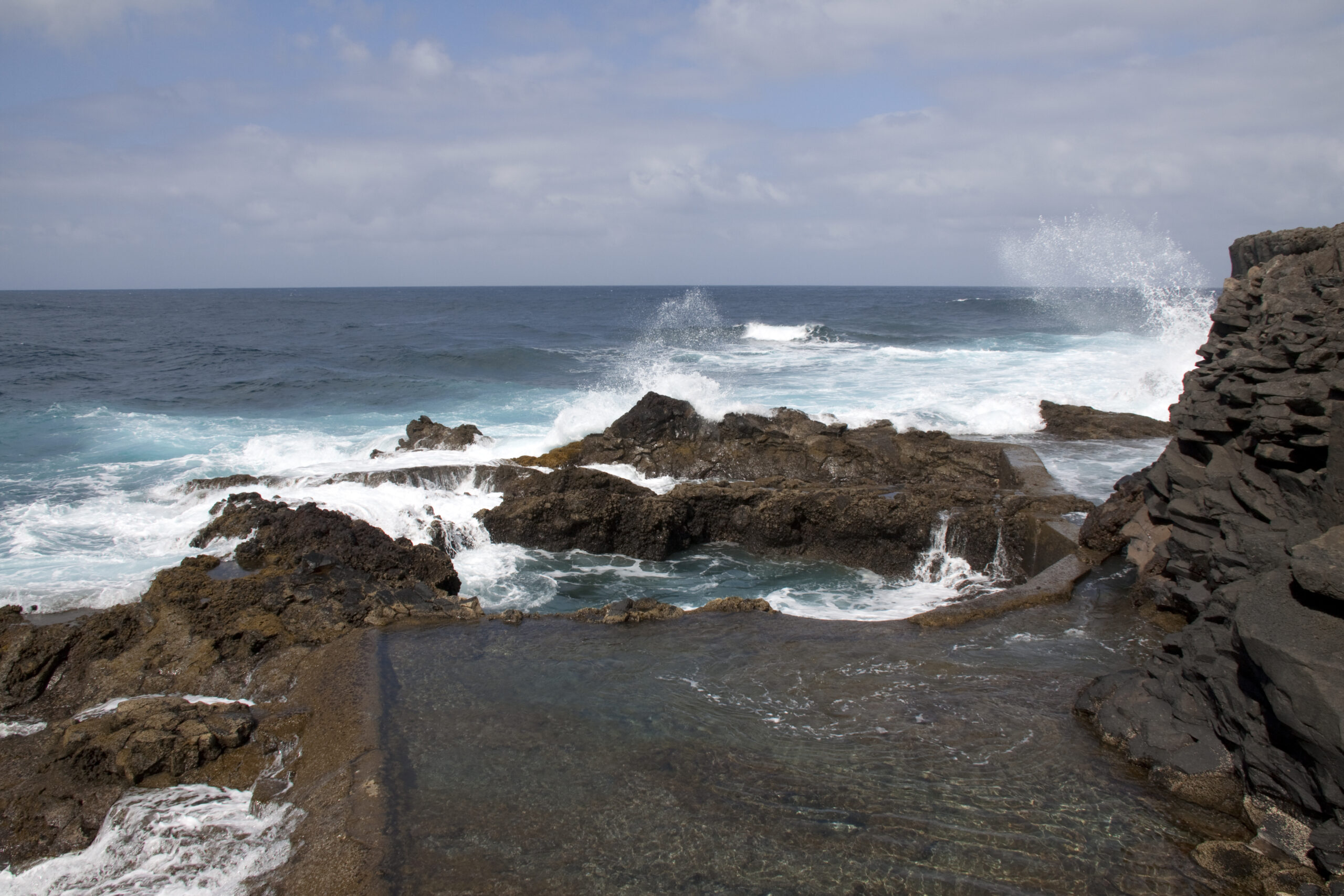 The dramatic Barlovento Coast features jagged volcanic rock formations and powerful Atlantic swells, with natural pools formed by the basalt landscape.