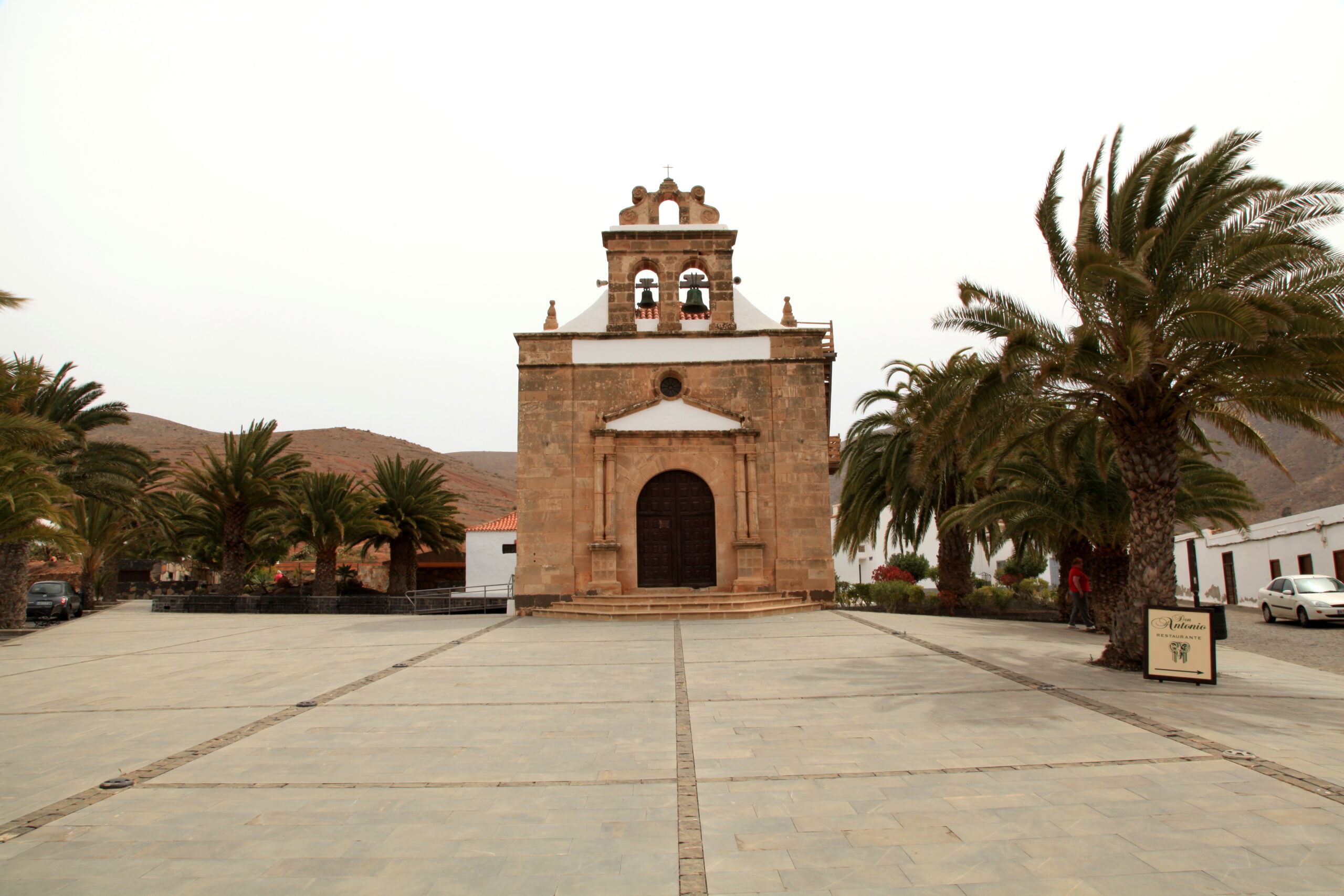 The historic stone church at Betancuria Old Town stands at the center of a peaceful plaza lined with palm trees.