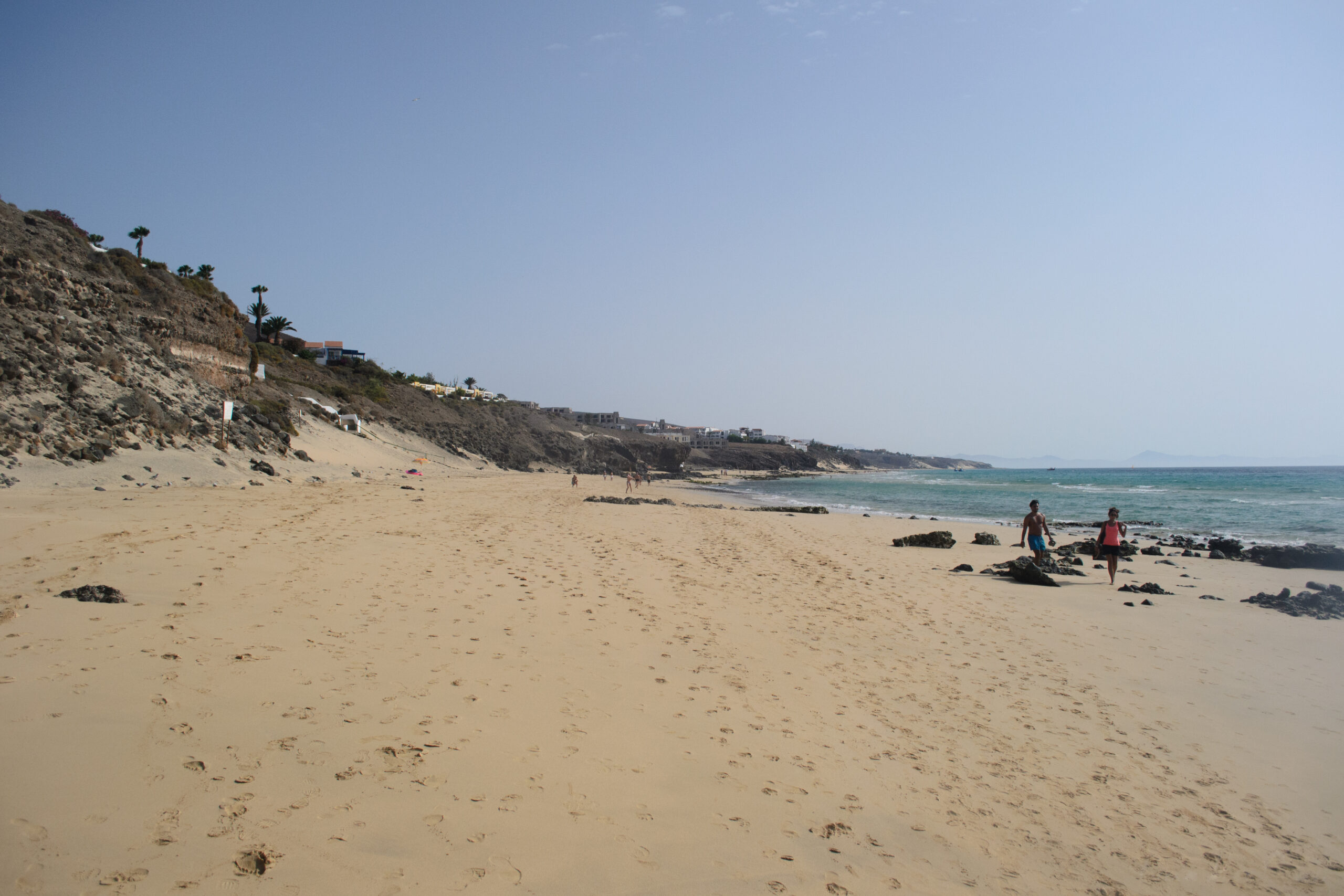 Butihondo Beach stretches along Jandía's coast with golden sand, shallow turquoise waters, and residential development built into the hillside.