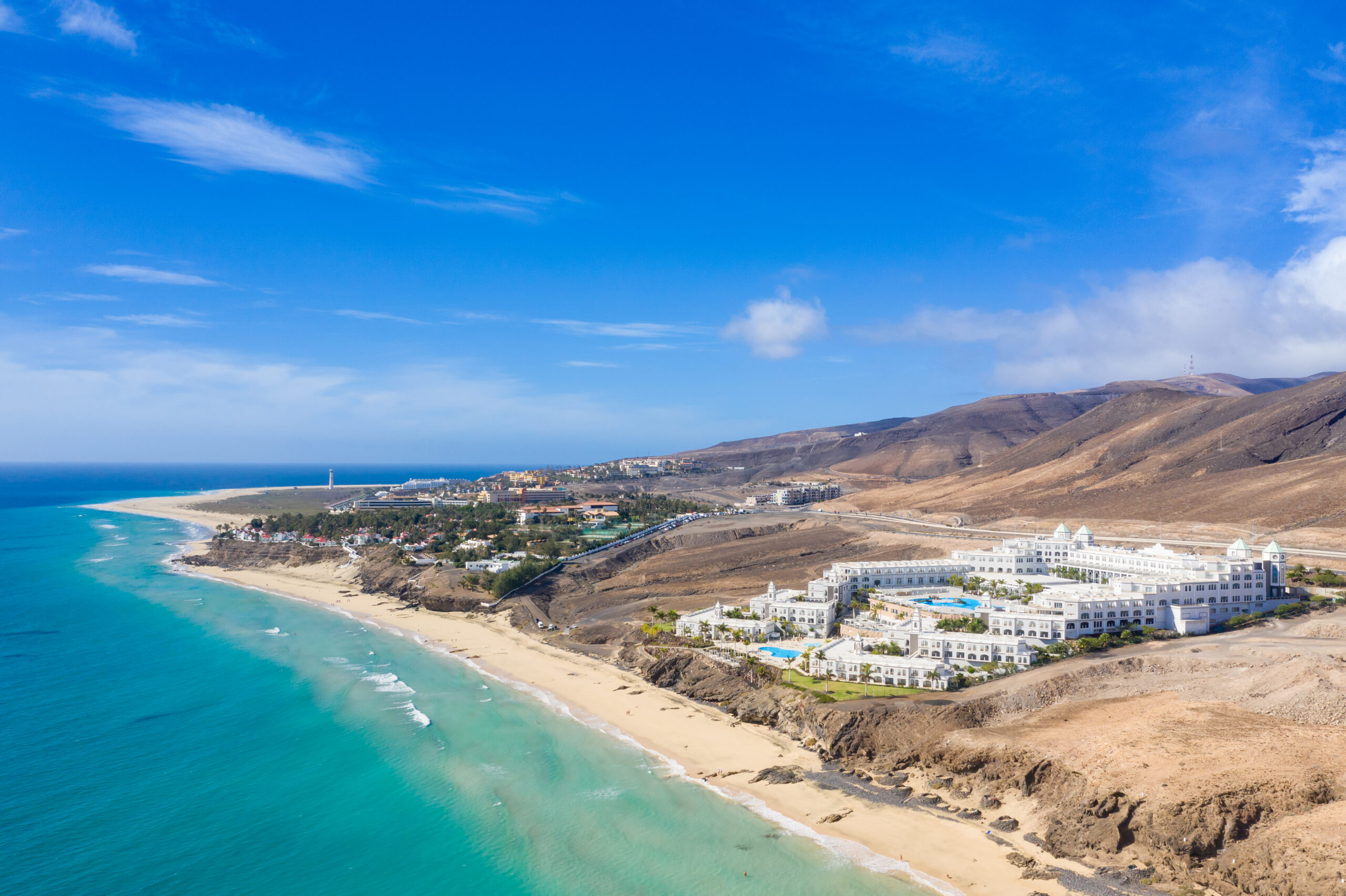 Butihondo Beach stretches along the Jandía peninsula with its pristine sand and turquoise waters, backed by modern resort developments set against the volcanic landscape.
