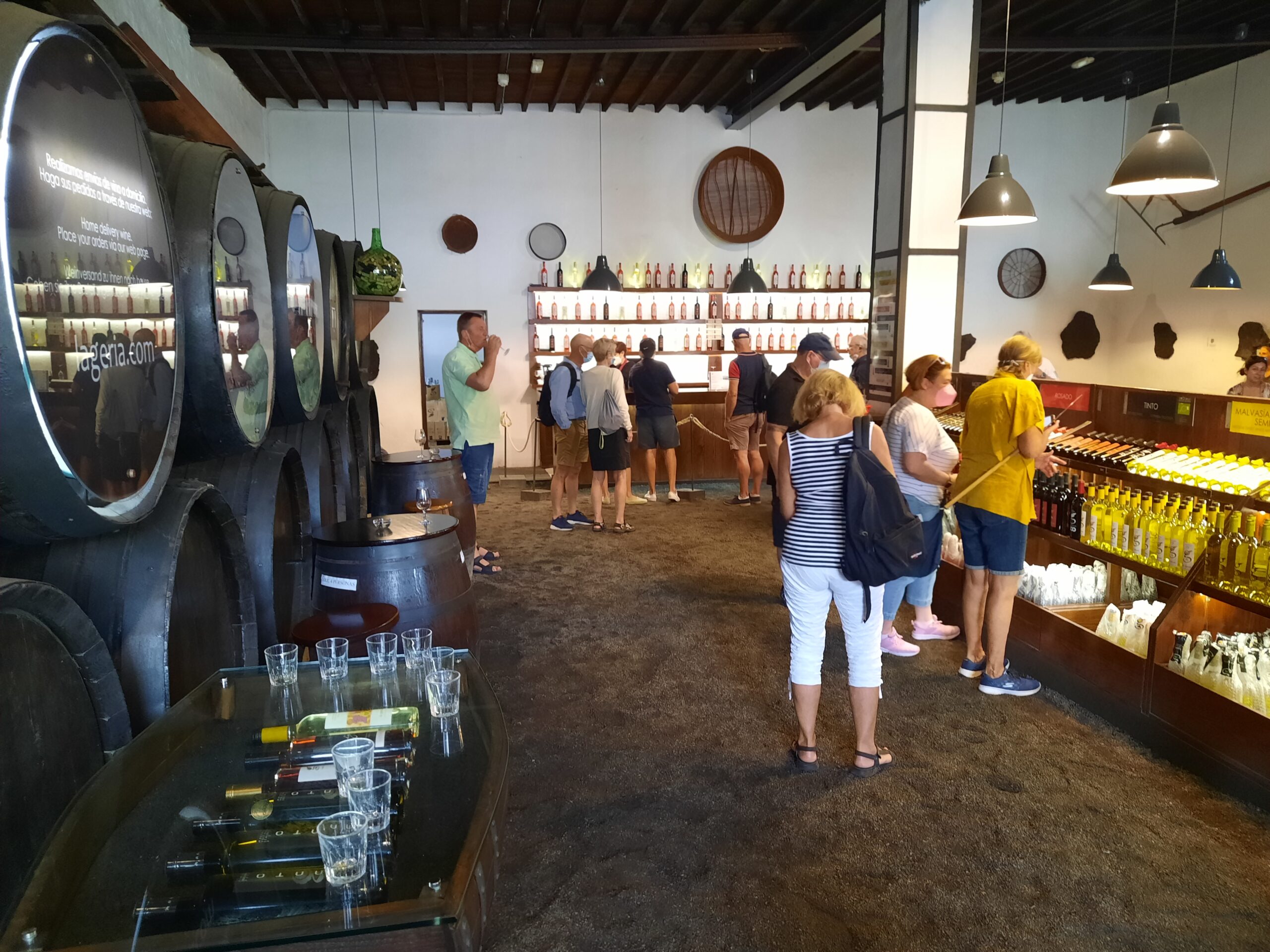 A modern winery tasting room displays local Canarian wines in bottles and serves visitors at a barrel-lined counter.