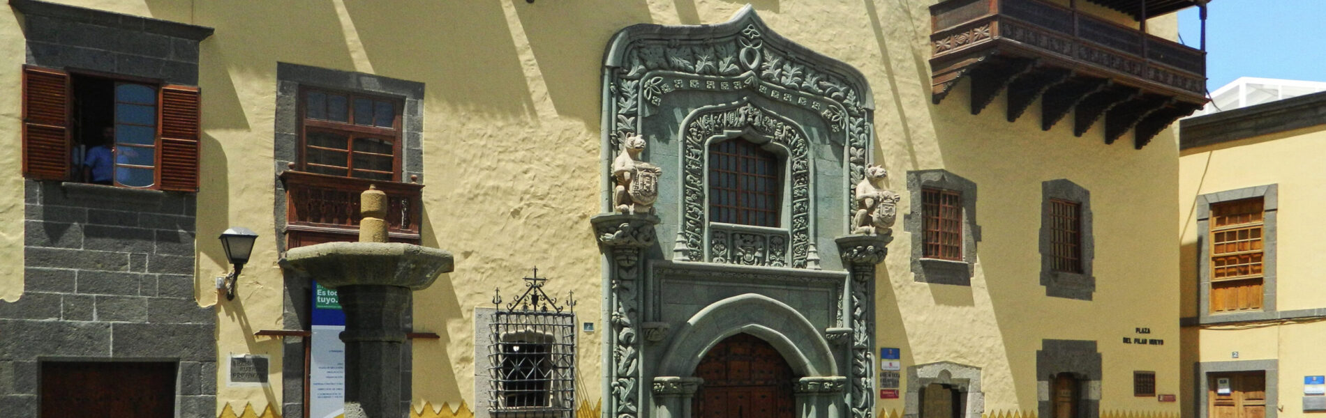 Colonial façade with carved stone doorway, wooden balconies and ochre walls facing a cobbled plaza.
