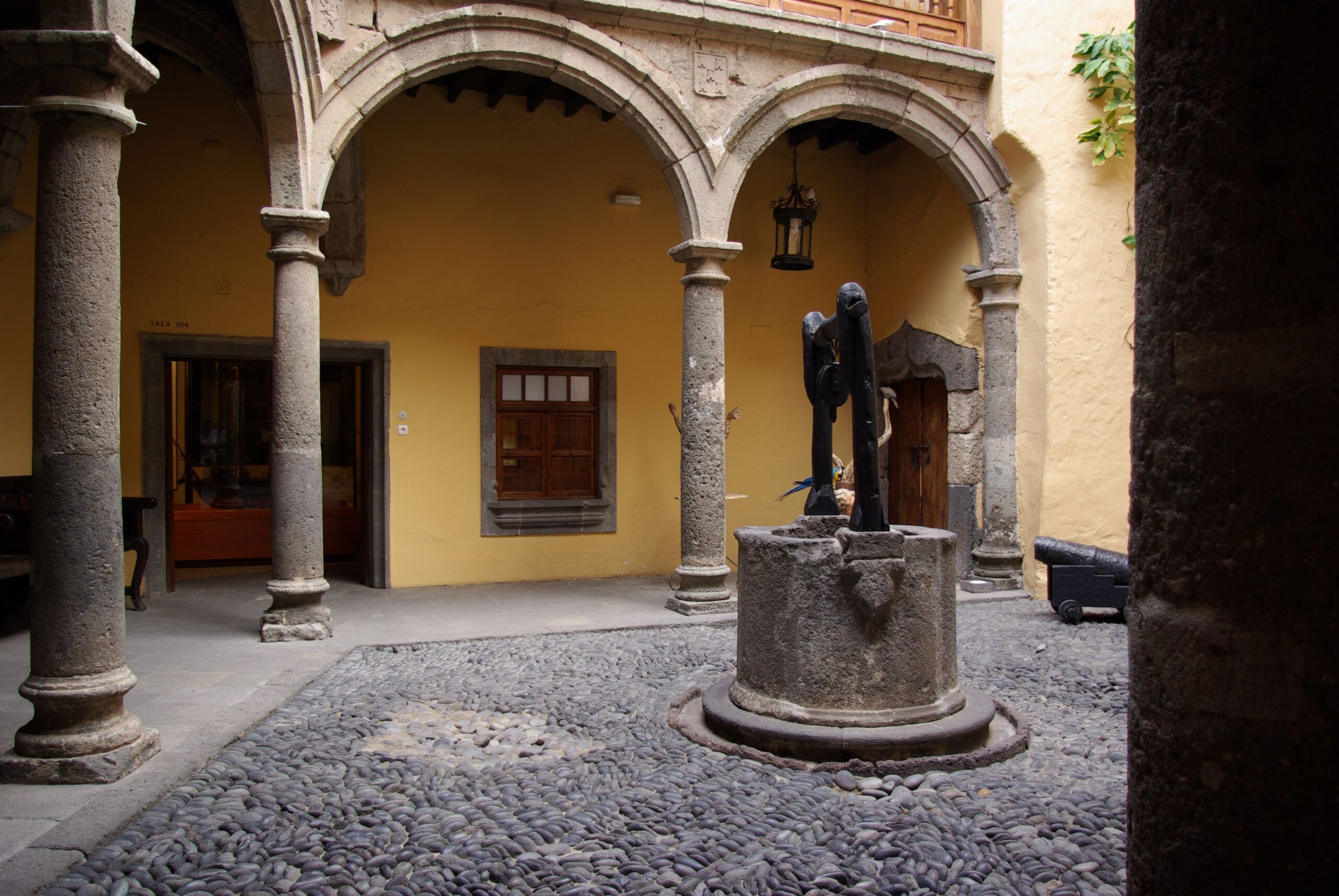 The courtyard of Casa de Colón features Renaissance arches, stone columns and traditional wooden balconies surrounding a central well.