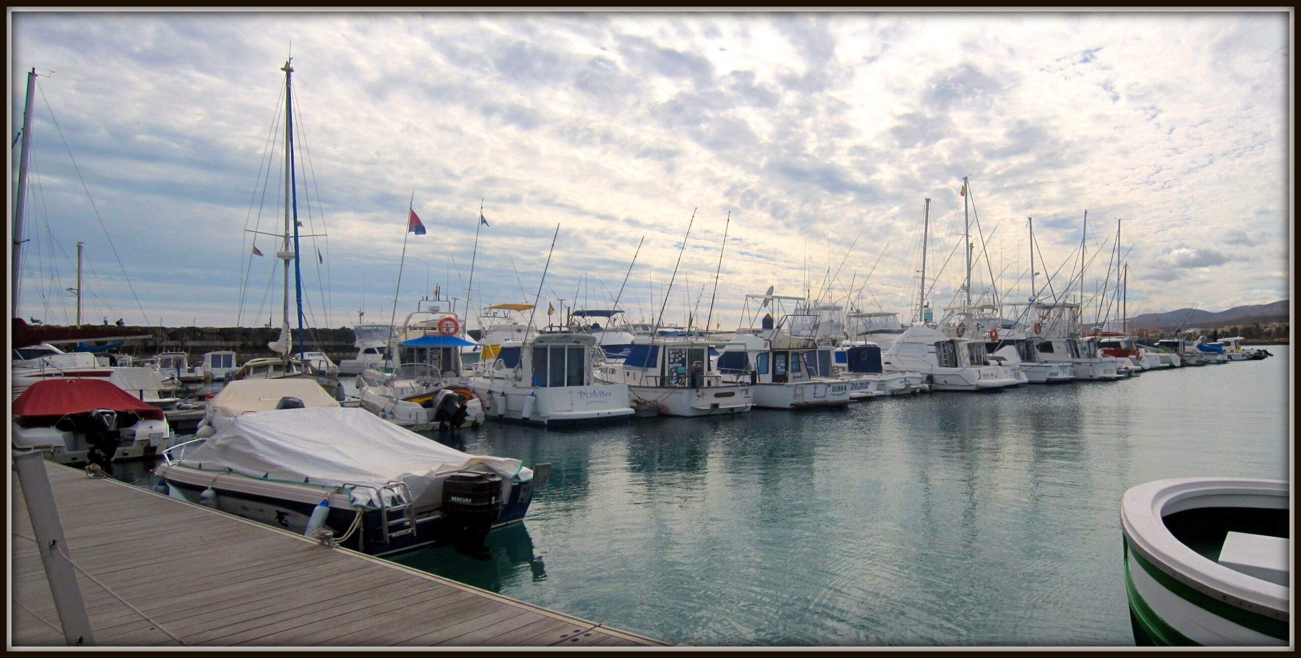 The sheltered marina at Caleta de Fuste features a fleet of recreational sailboats and working vessels alongside the dock.