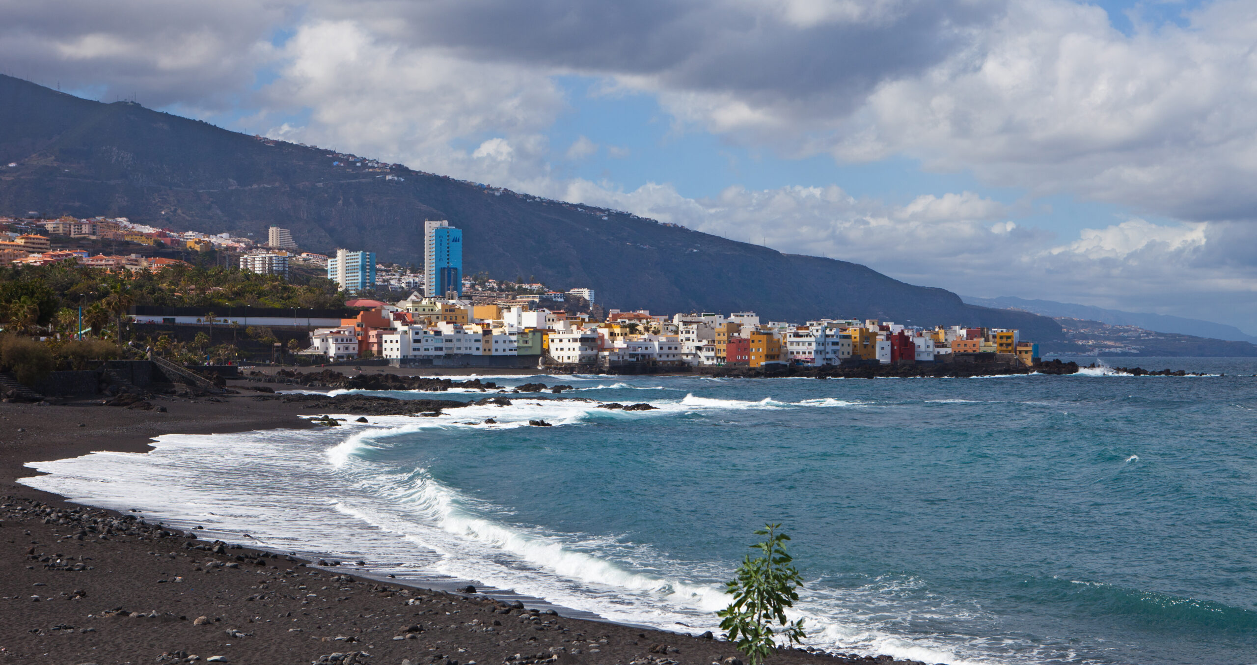 Puerto de la Cruz spreads along the northern coast of Tenerife, with its characteristic colorful architecture set against dramatic volcanic slopes and the Atlantic Ocean.