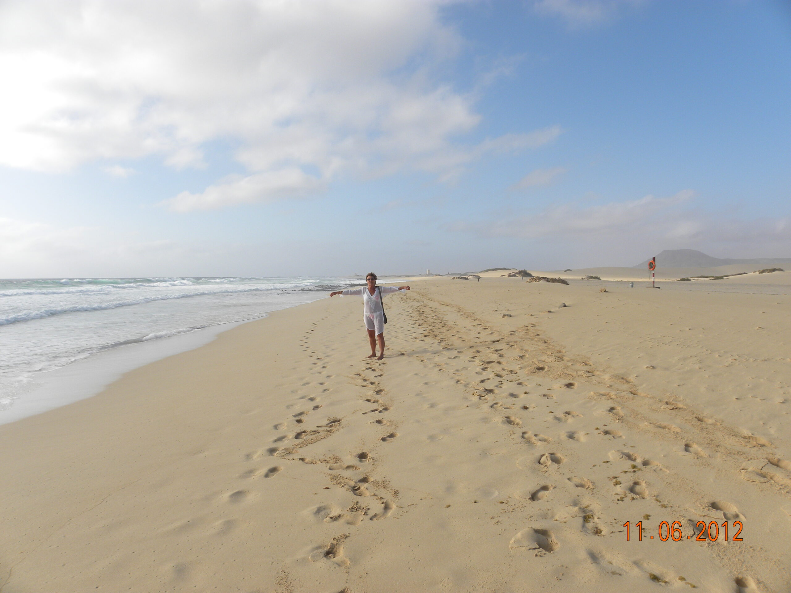 The expansive sandy beach at Corralejo Dunes offers a serene stretch of golden sand meeting shallow Atlantic waters, with distinctive dunes rising in the background.
