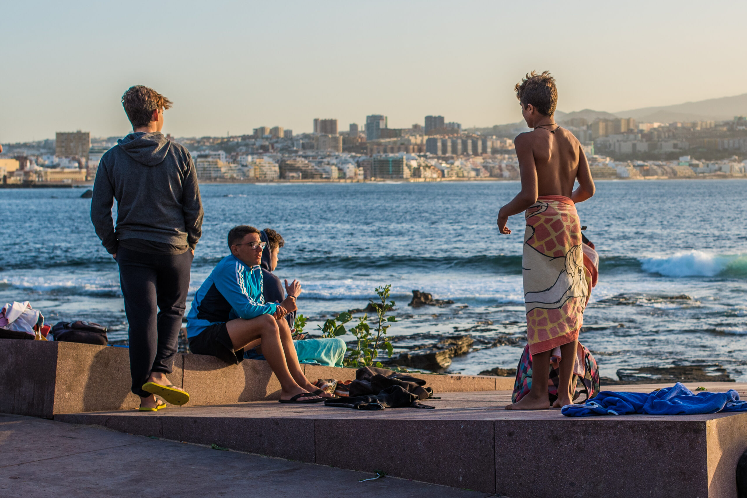 Visitors enjoy the El Confital waterfront with views across the bay towards the urban skyline of Las Palmas.