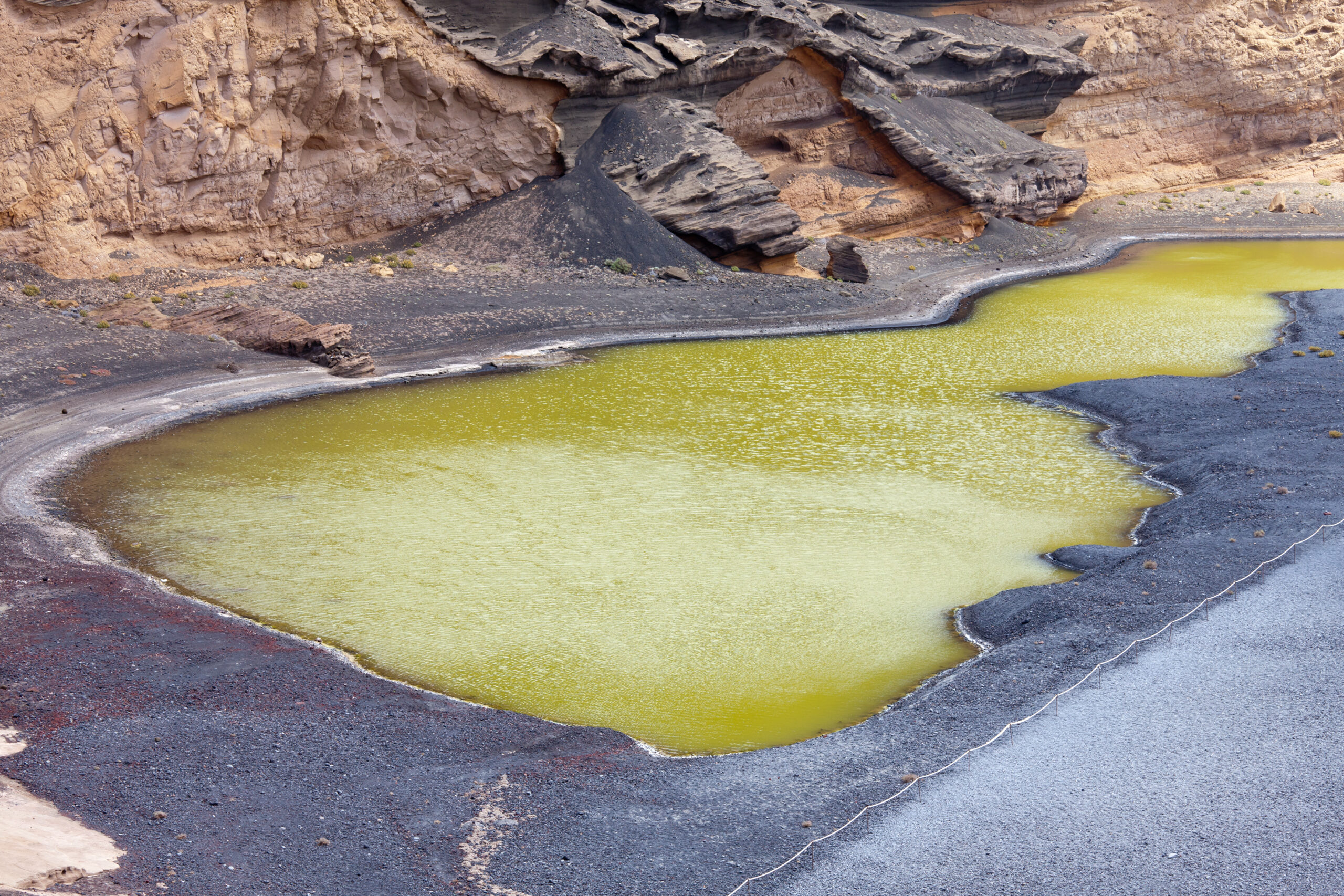 The striking yellow-green waters of Charco de los Clicos, formed by mineral-rich volcanic deposits and algae growth, contrast sharply with the surrounding dark lava fields and sandy cliffs.