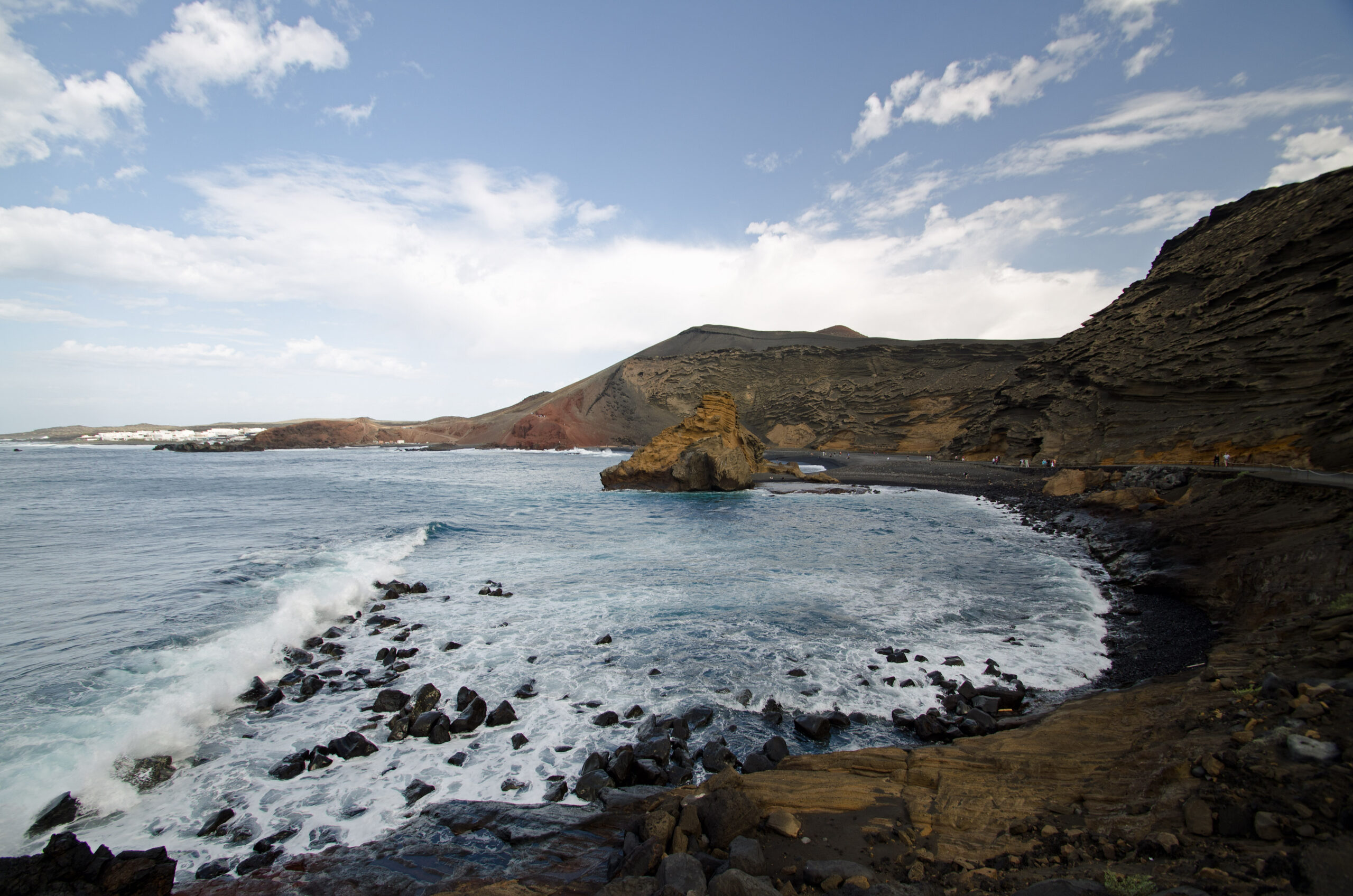 The dramatic volcanic landscape of El Golfo features dark basalt cliffs framing a sheltered cove with distinctive golden and ochre-colored rock formations.