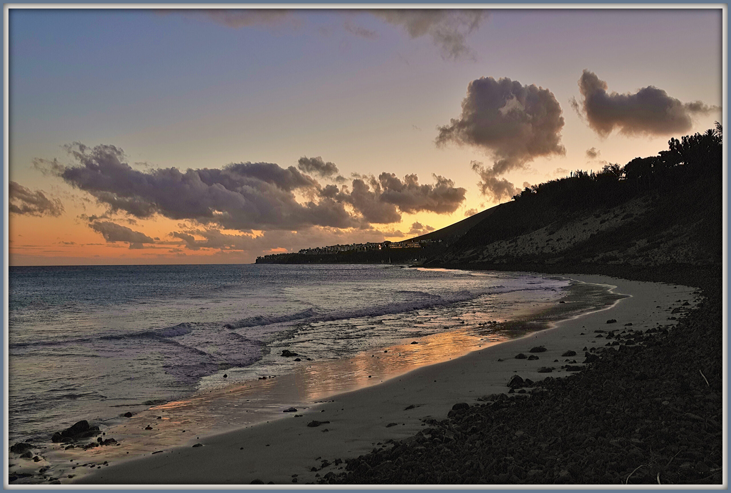 Esquinzo Beach glows in golden light during sunset, with volcanic cliffs rising above the sand and calm Atlantic waters.