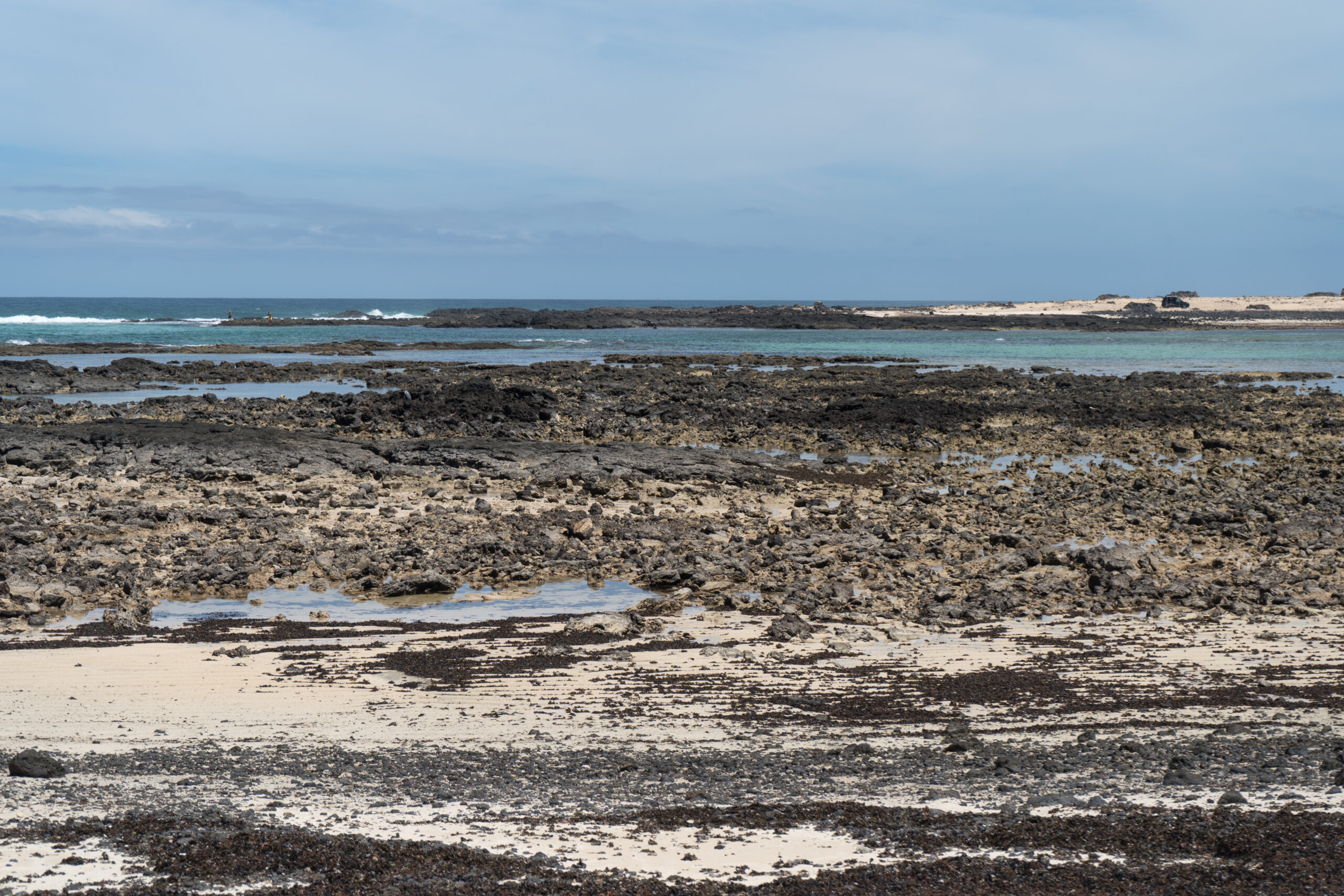 The dramatic rocky coast near Faro del Tostón features volcanic formations, clear turquoise waters, and pristine sandy beaches characteristic of El Cotillo's natural landscape.