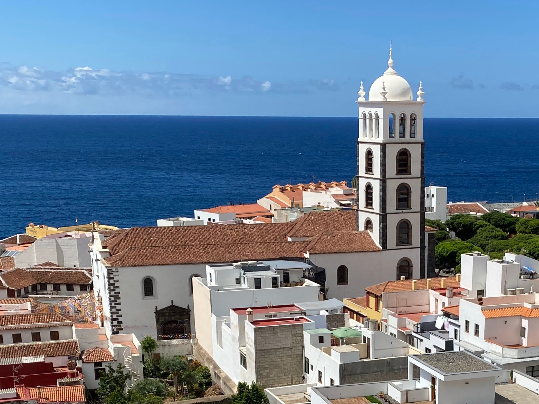White church with domed bell tower overlooking terracotta-roofed buildings and blue Atlantic Ocean under clear sky
