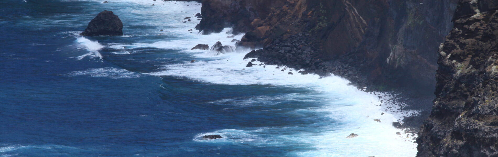 Dramatic rocky coastline with dark volcanic cliffs and turquoise waves crashing against jagged rocks and boulders