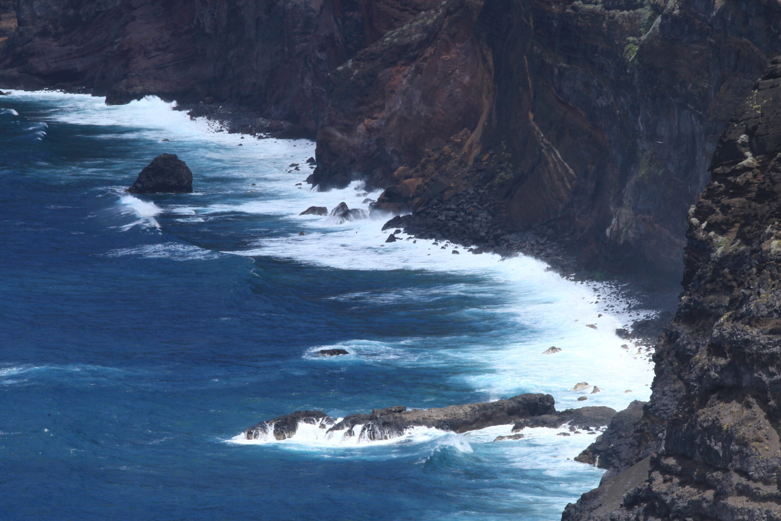 The rugged Garafía Coast features steep volcanic cliffs and powerful Atlantic swells breaking against dark basalt rock formations.