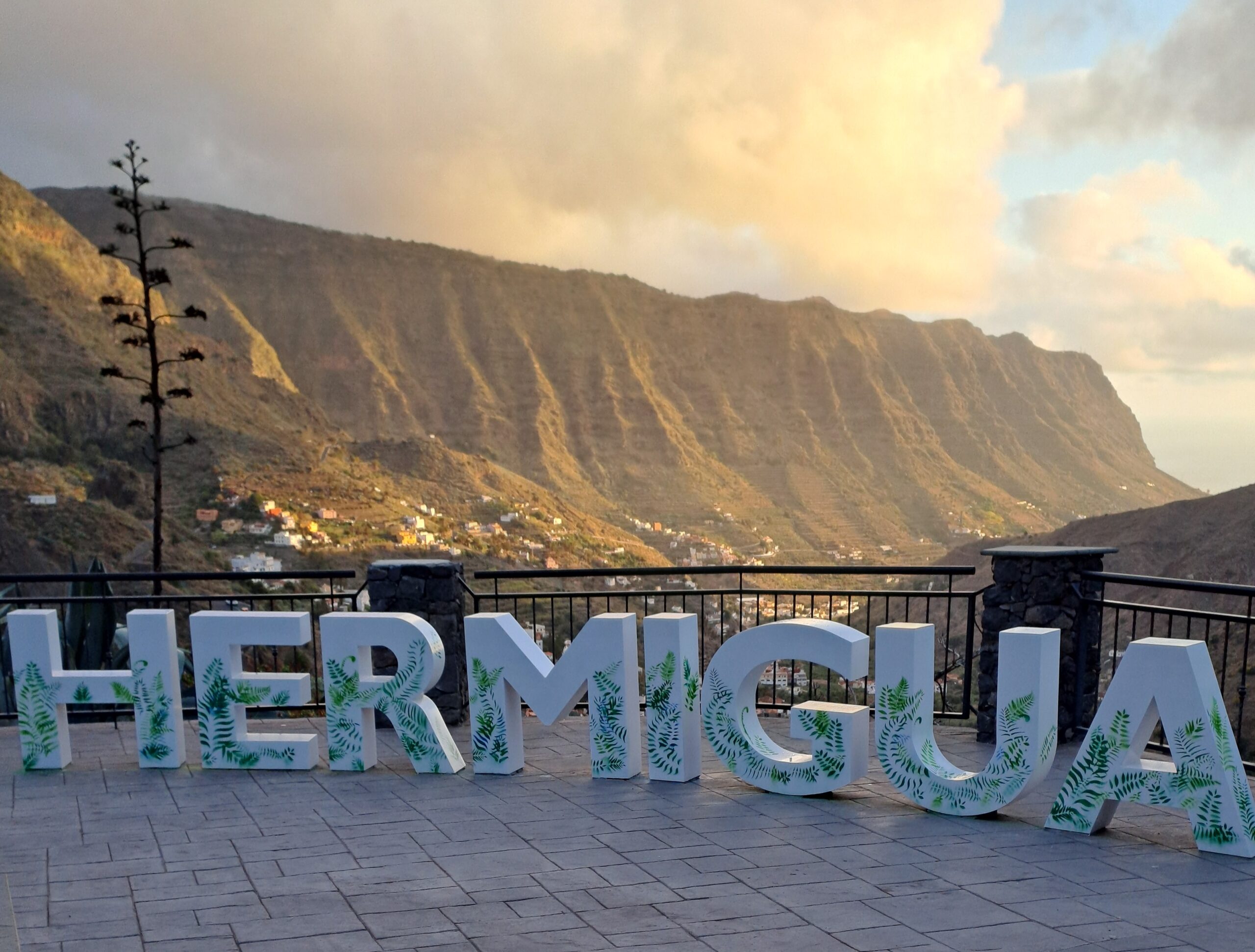 The Hermigua Valley sign frames one of La Gomera’s most striking natural features—steep, deeply grooved cliffs rising above the town nestled in the valley below.