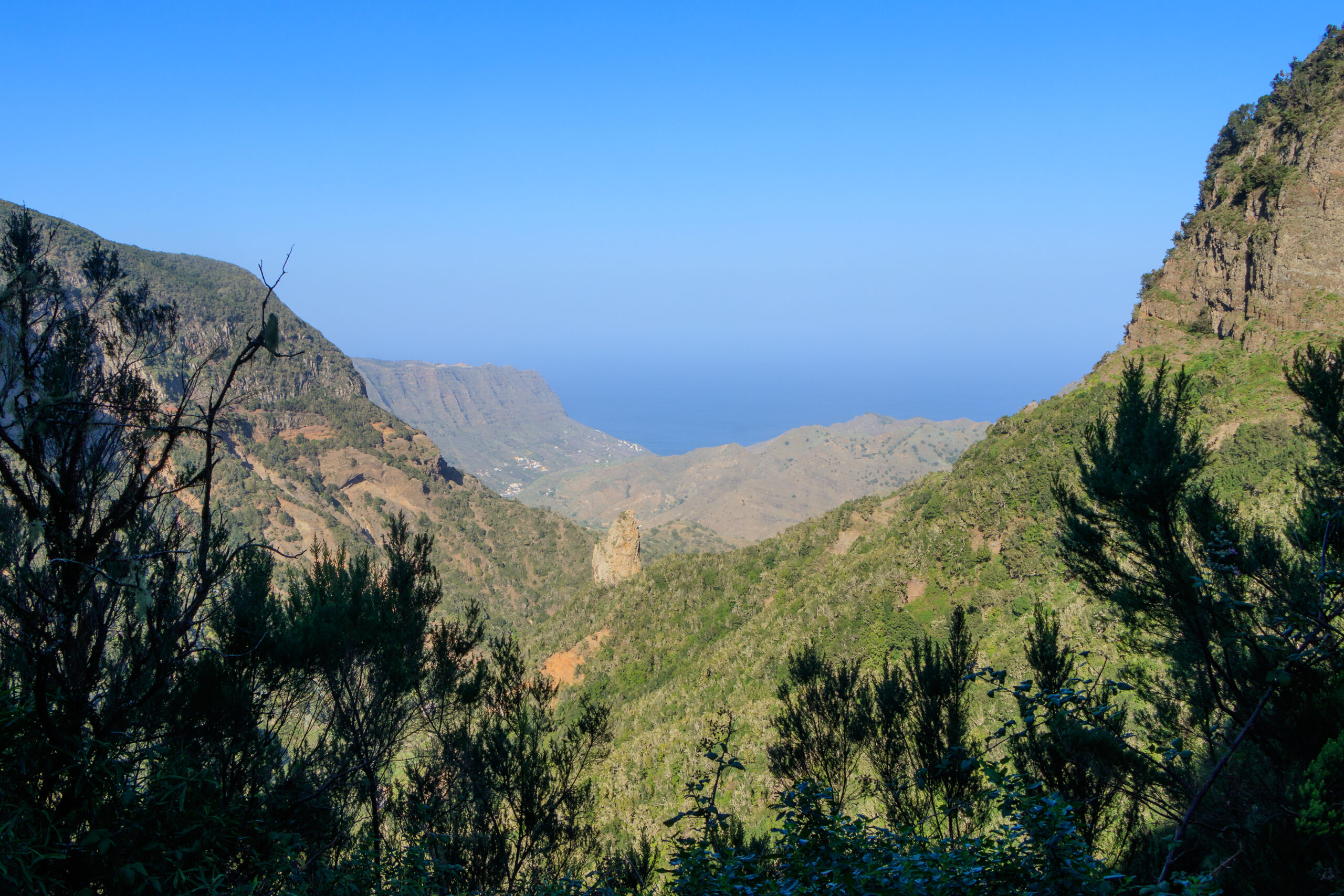 The Hermigua Valley displays the dramatic topography of La Gomera, with steep laurel forest-covered cliffs framing the fertile valley and views toward the coast.