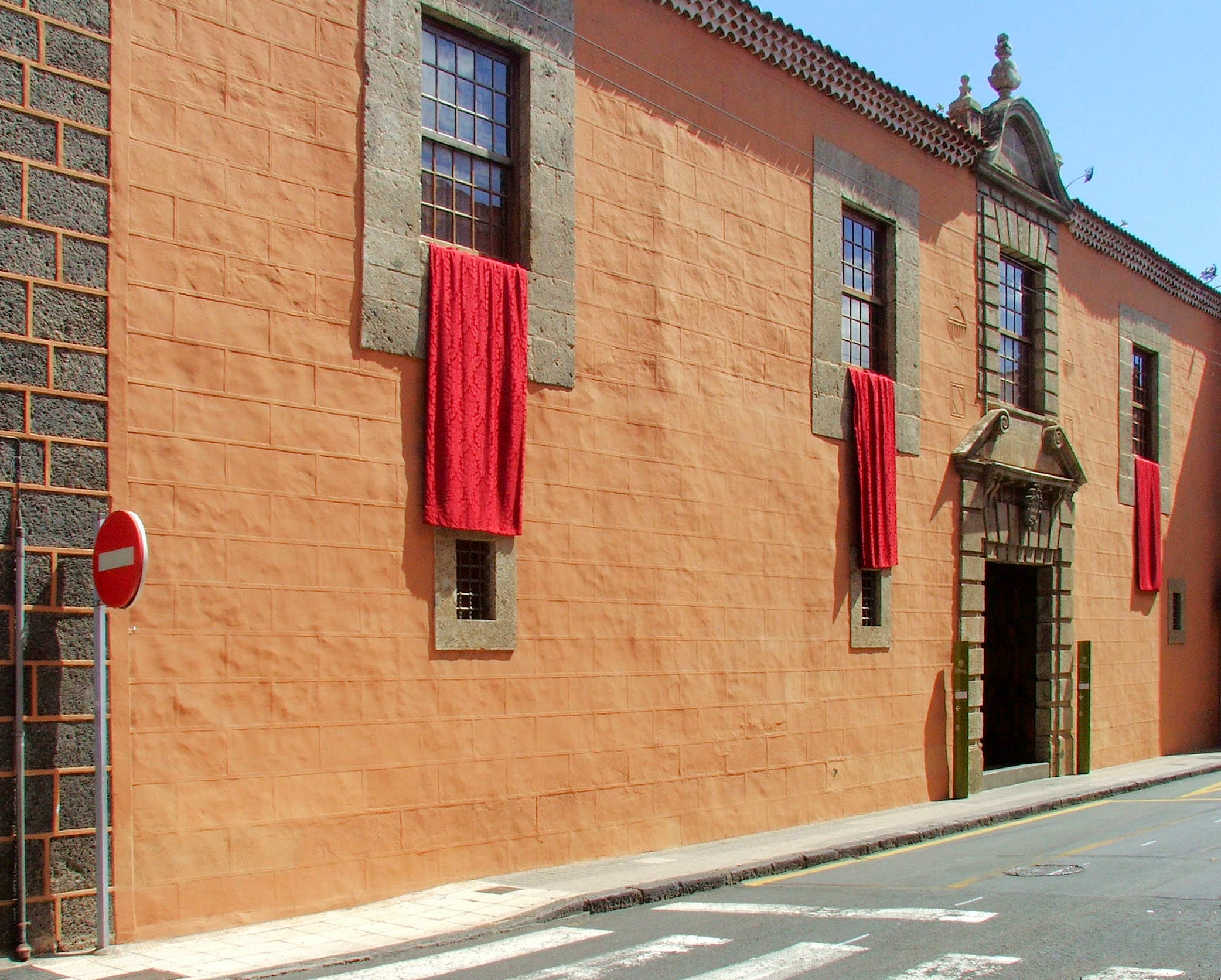 Terracotta-colored colonial building with stone trim, red fabric banners draped from windows, and a decorative entrance portal.