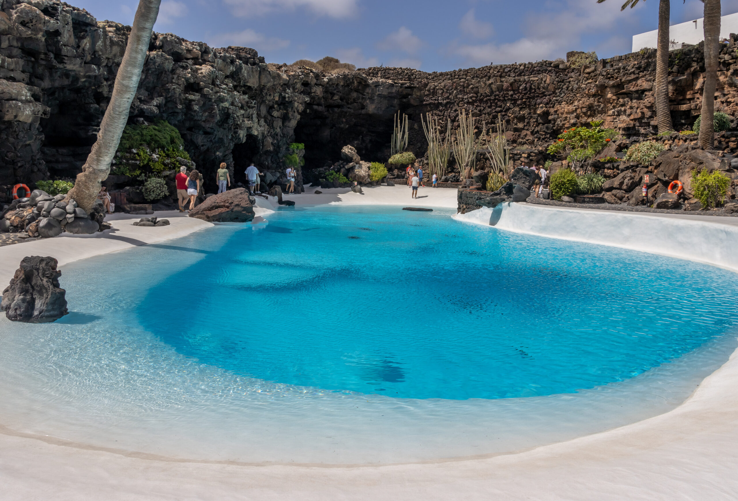 The stunning lagoon at Jameos del Agua, where crystal-clear turquoise waters meet pristine white sand framed by dramatic volcanic rock formations.