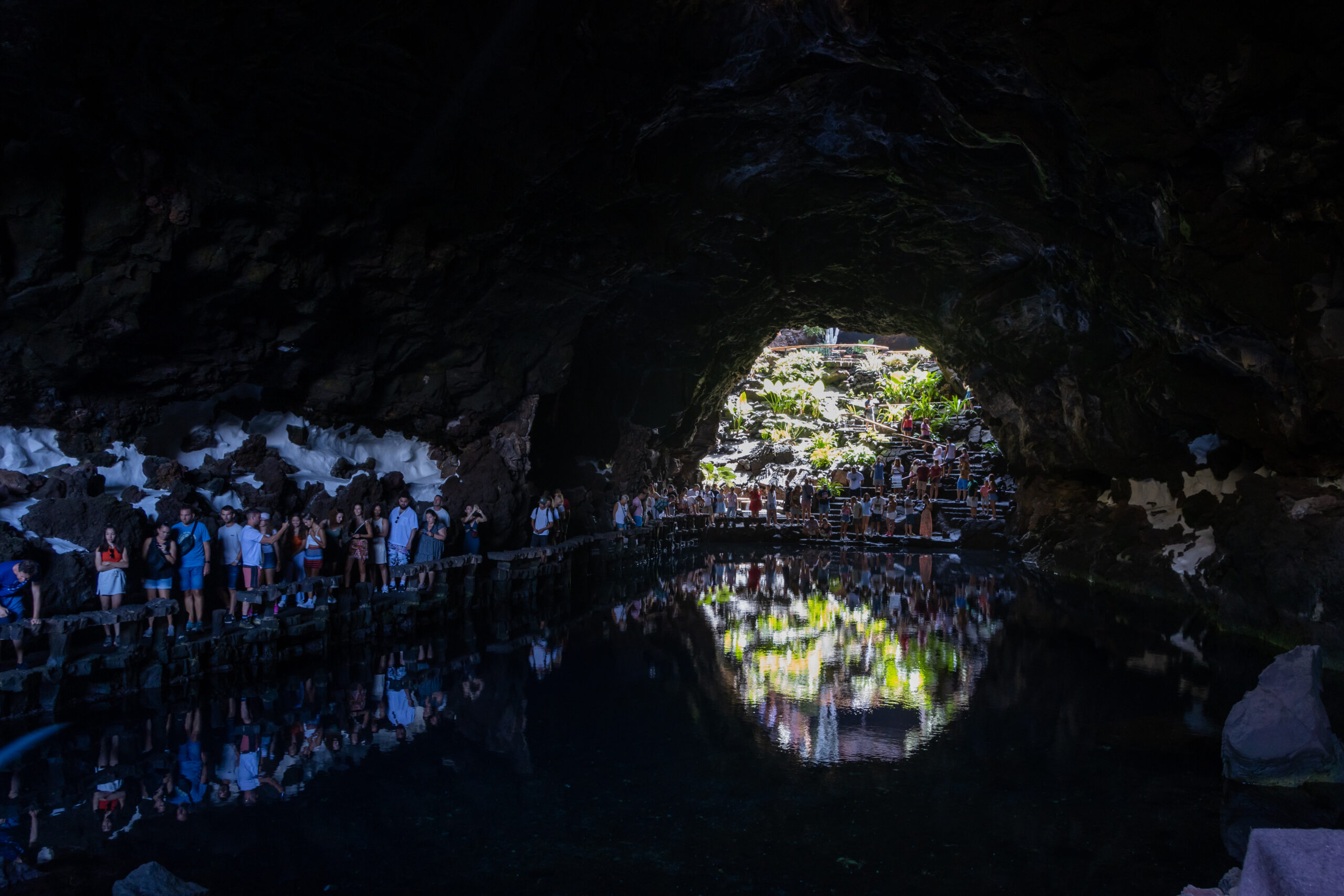 Visitors explore the dramatic underground lake chamber at Jameos del Agua, where natural caverns frame views of the sunlit terraces and lush surroundings beyond.