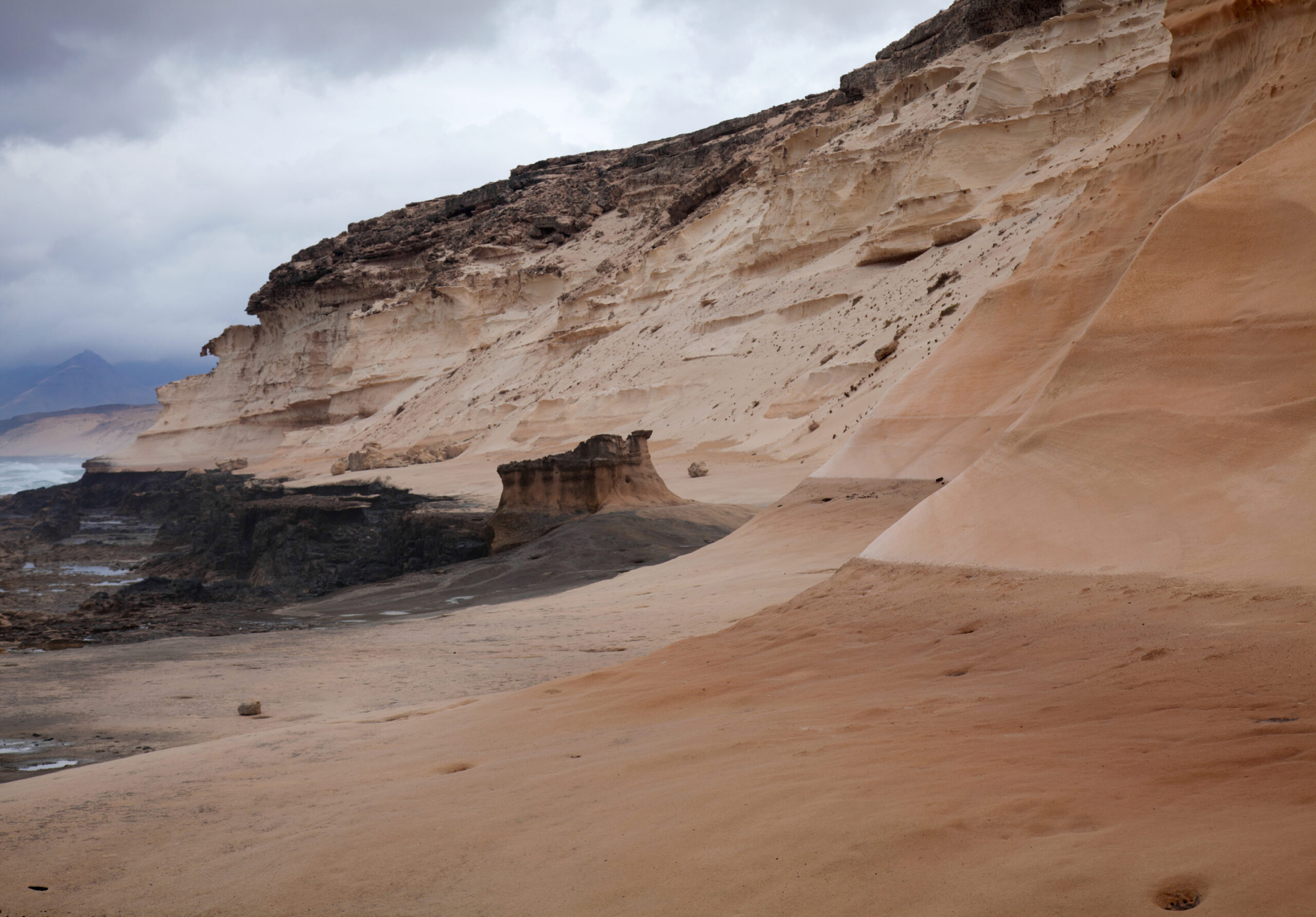 Dramatic coastal cliffs in Jandía Natural Park display layered geological formations where sand and volcanic rock meet the shoreline.