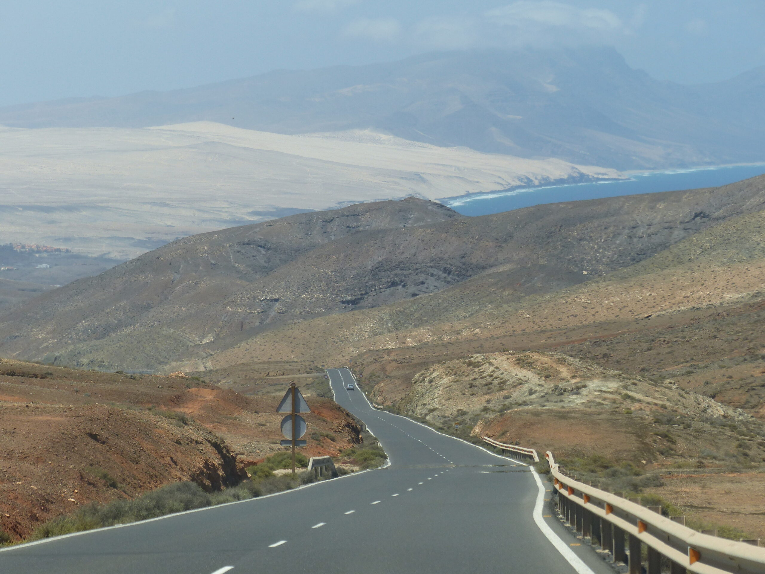 A scenic mountain road curves through the volcanic landscape of Jandía Natural Park, offering views across the peninsula toward the coastline.