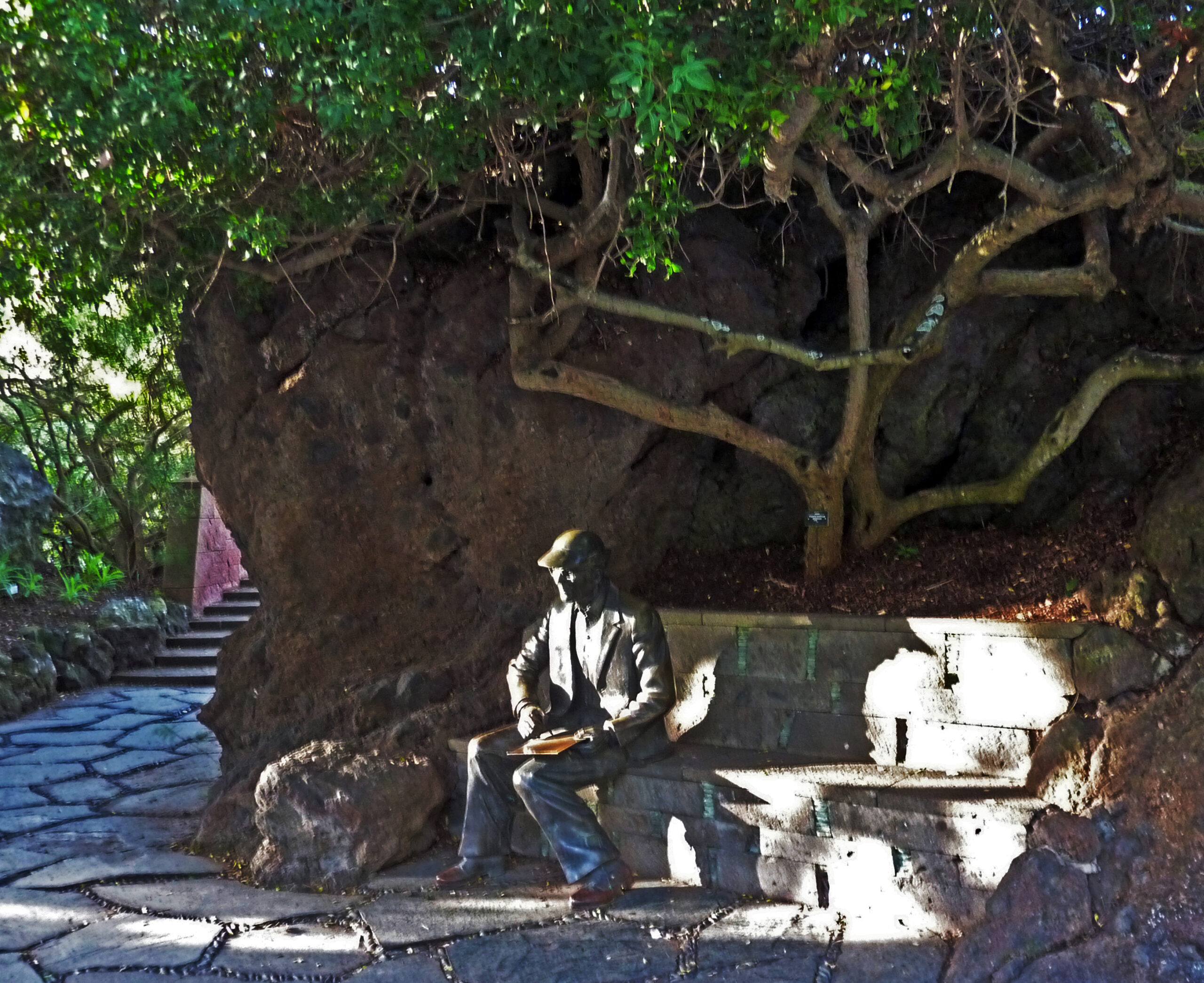 A statue honoring Eric R. Sventenius, the botanist who founded the Jardín Botánico Canario, sits sheltered beneath a mature tree within the garden grounds.