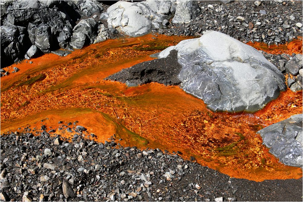 Vivid mineral-rich waters create striking orange streaks across the volcanic terrain of La Palma's mountainous landscape.