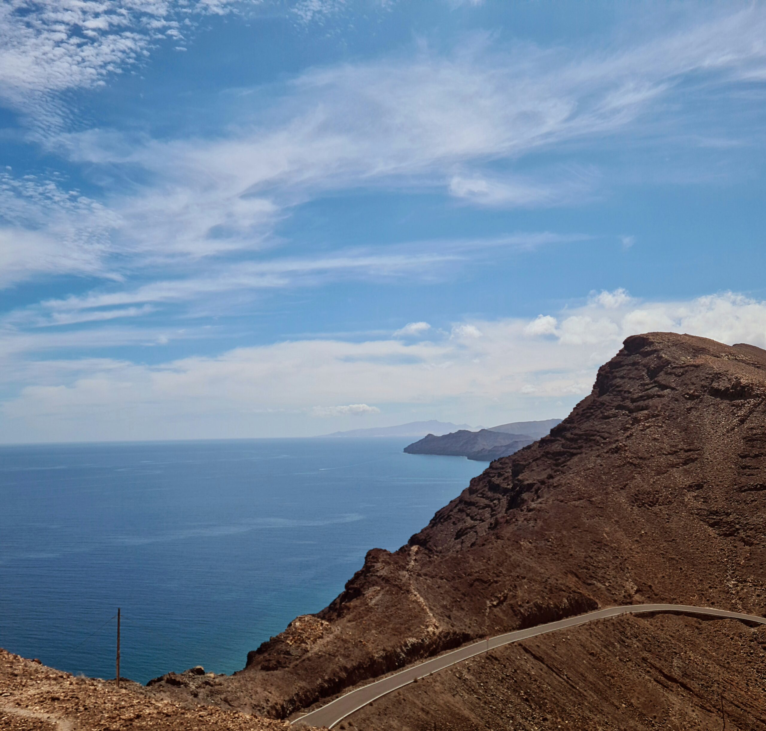 A winding road hugs the dramatic volcanic cliffs above the Atlantic, offering sweeping views toward neighboring islands.