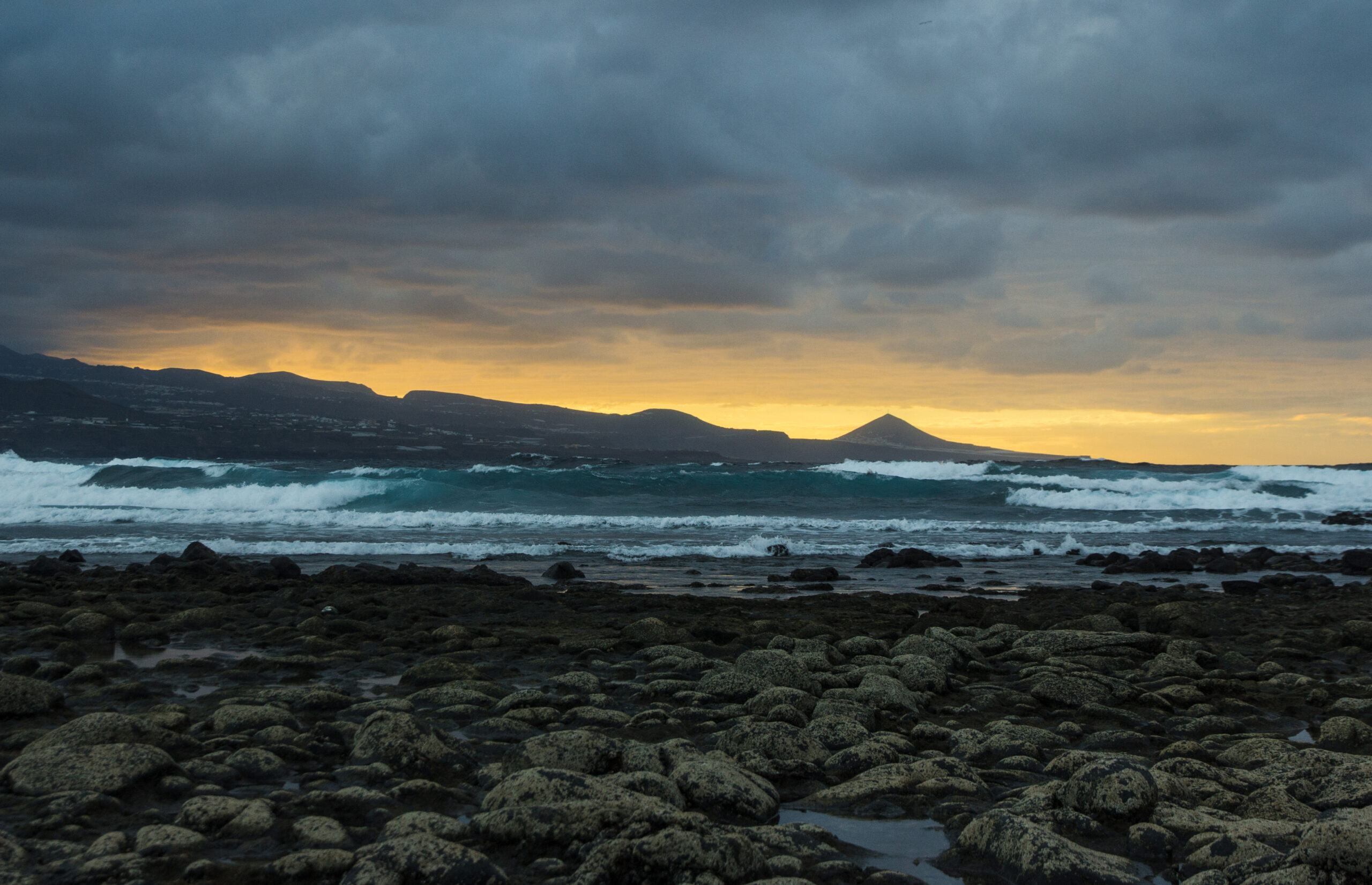 A sunset view across La Isleta’s volcanic coastline, with cone-shaped peaks rising beyond the surf.