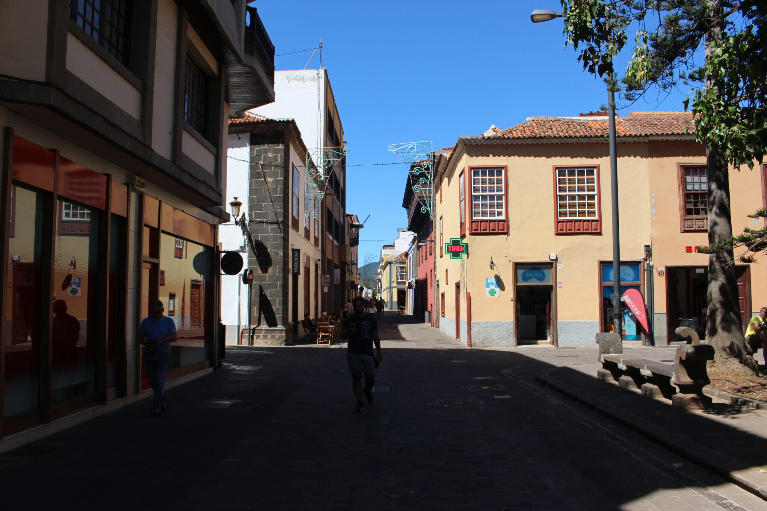 Sunlit cobblestone street lined with colorful colonial buildings featuring wooden balconies and shutters in La Laguna's historic old town.