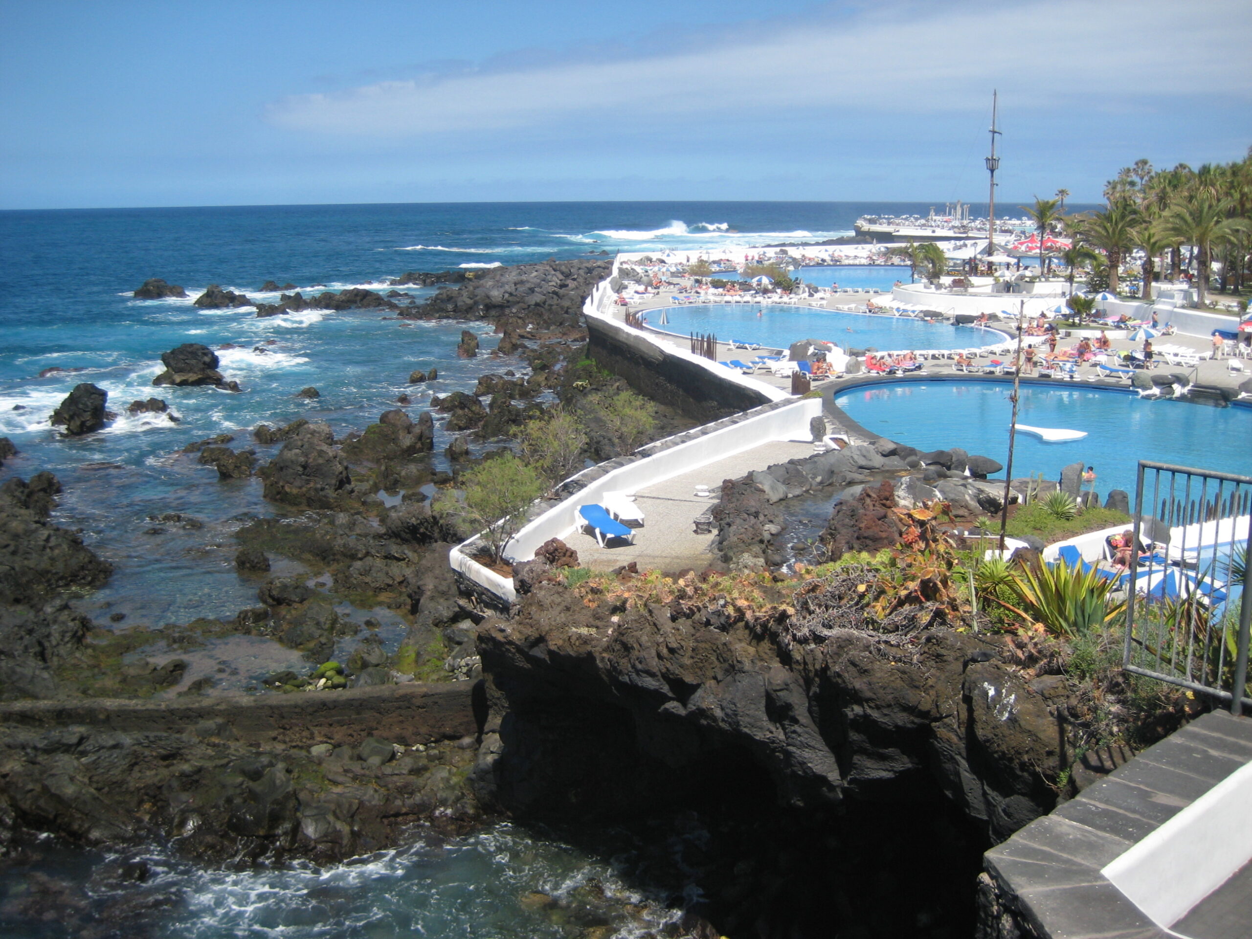 Lago Martiánez in Puerto de la Cruz features striking artificial pools built into the volcanic landscape, offering a dramatic contrast between the vibrant blue water and rugged black lava formations.