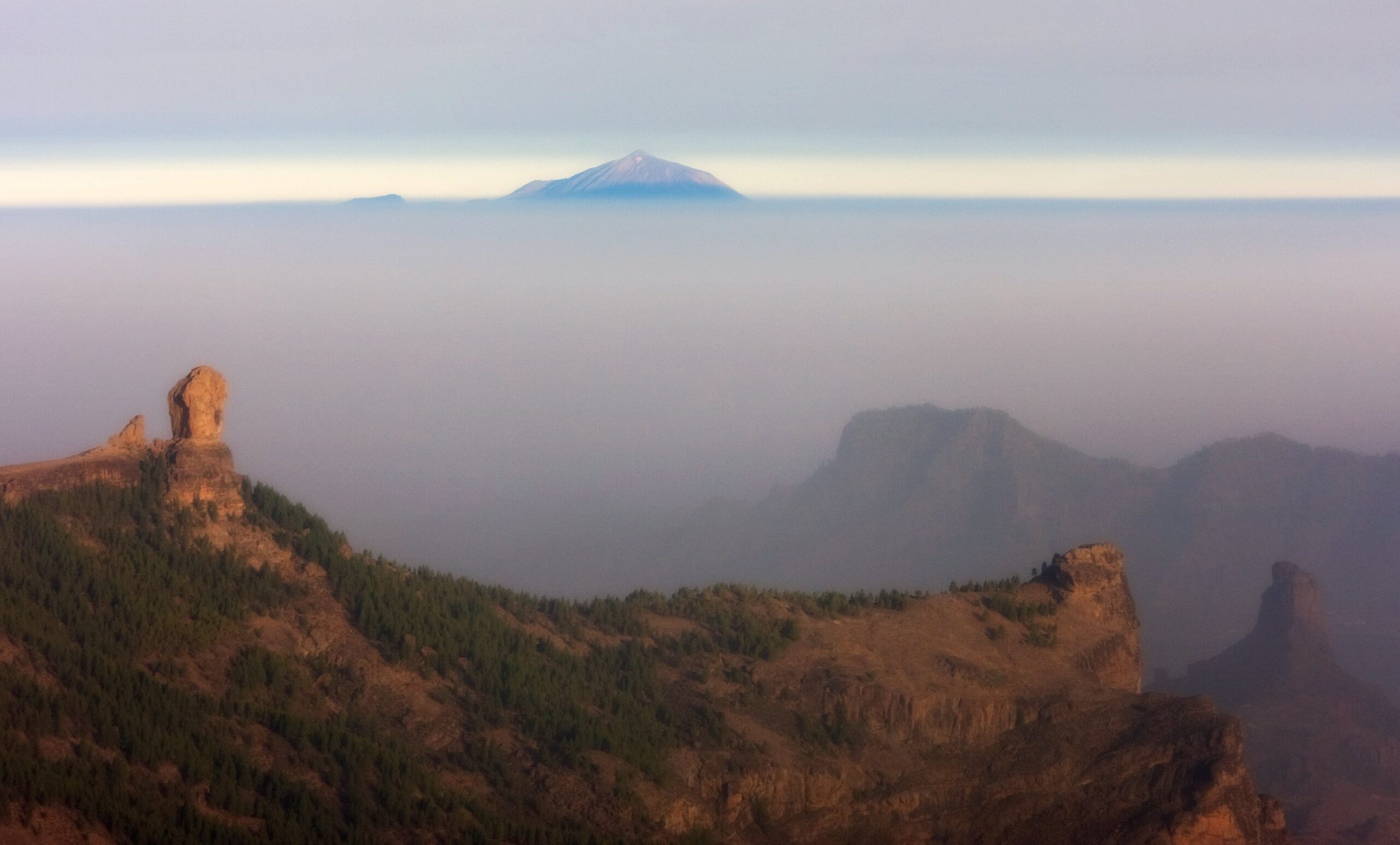 The dramatic landscape of Llanos de la Pez frames a distant volcanic peak above the cloud layer, bathed in early morning light.