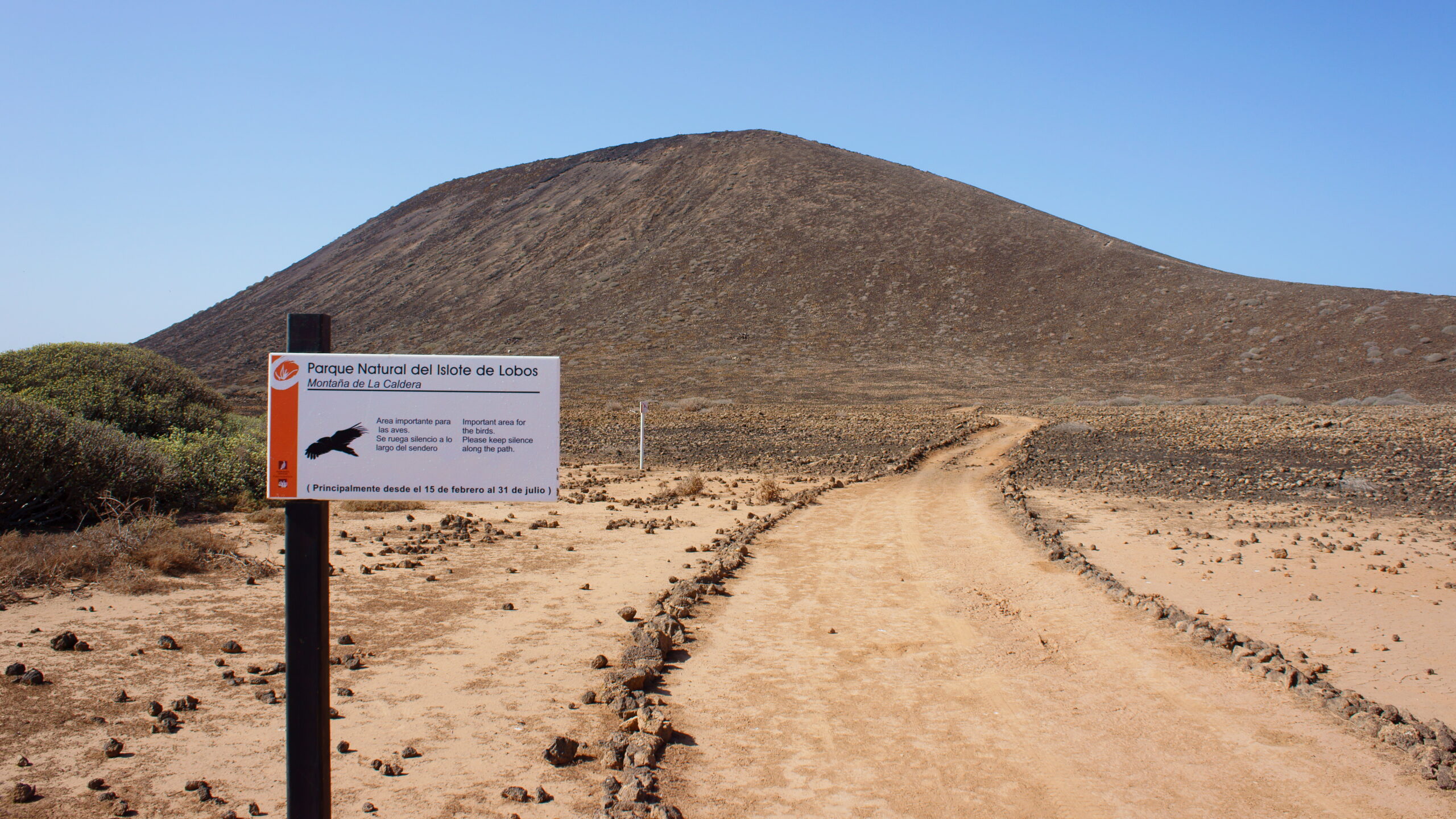 The entrance to Lobos Island Natural Park features a distinctive volcanic cone and sandy track leading into the protected reserve.