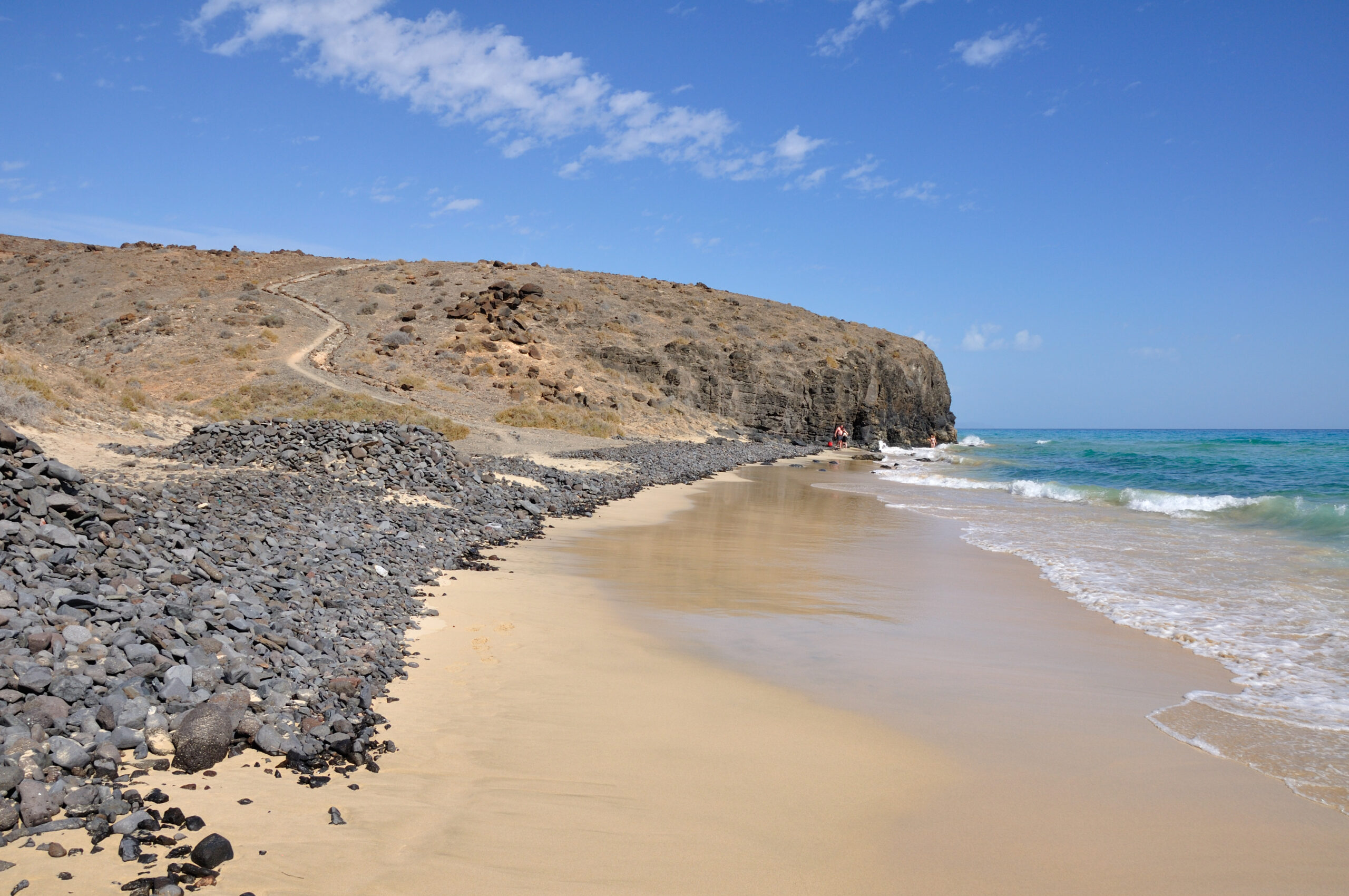 Mal Nombre Beach features a sheltered sandy cove bordered by volcanic rock formations and dry hillsides overlooking the Atlantic.