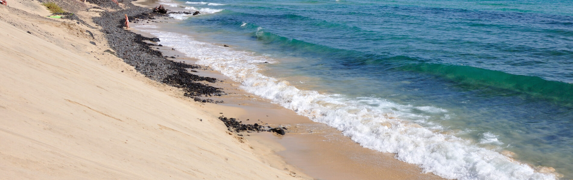 Sandy beach with gentle waves and turquoise water, backed by rocky cliffs under clear blue sky