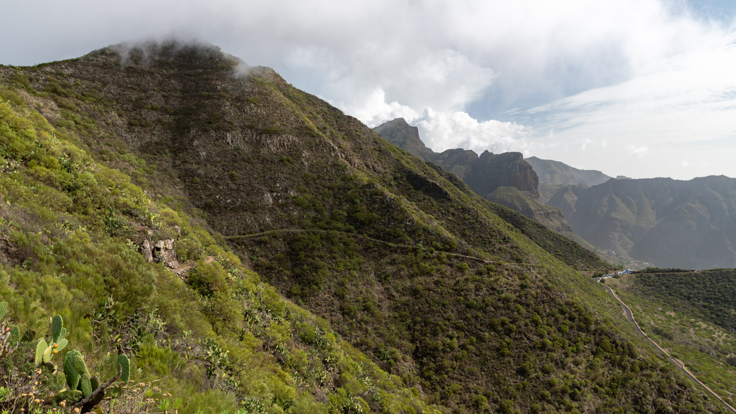 The dramatic terrain surrounding the Masca Trail in Tenerife features steep, vegetation-covered volcanic slopes and rugged mountain peaks.