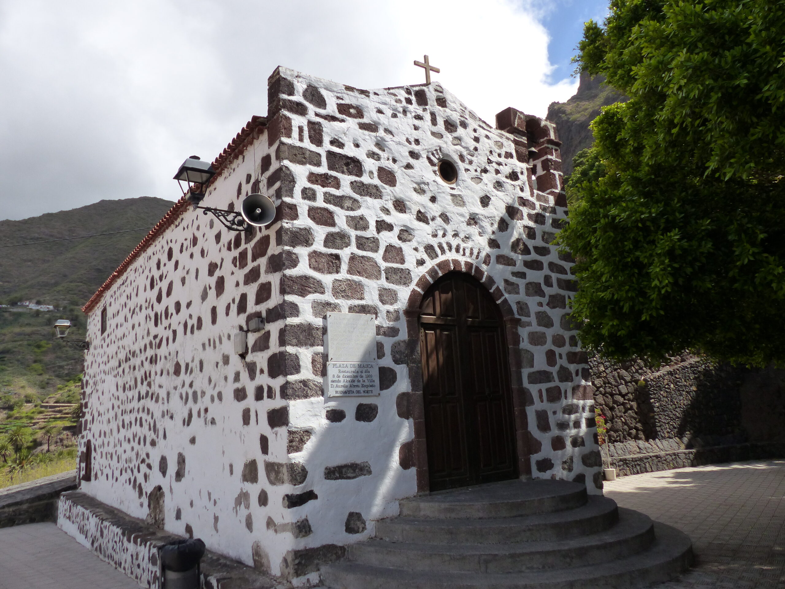 A traditional whitewashed stone chapel in Masca Village, built with dark volcanic stone and topped with a wooden cross.