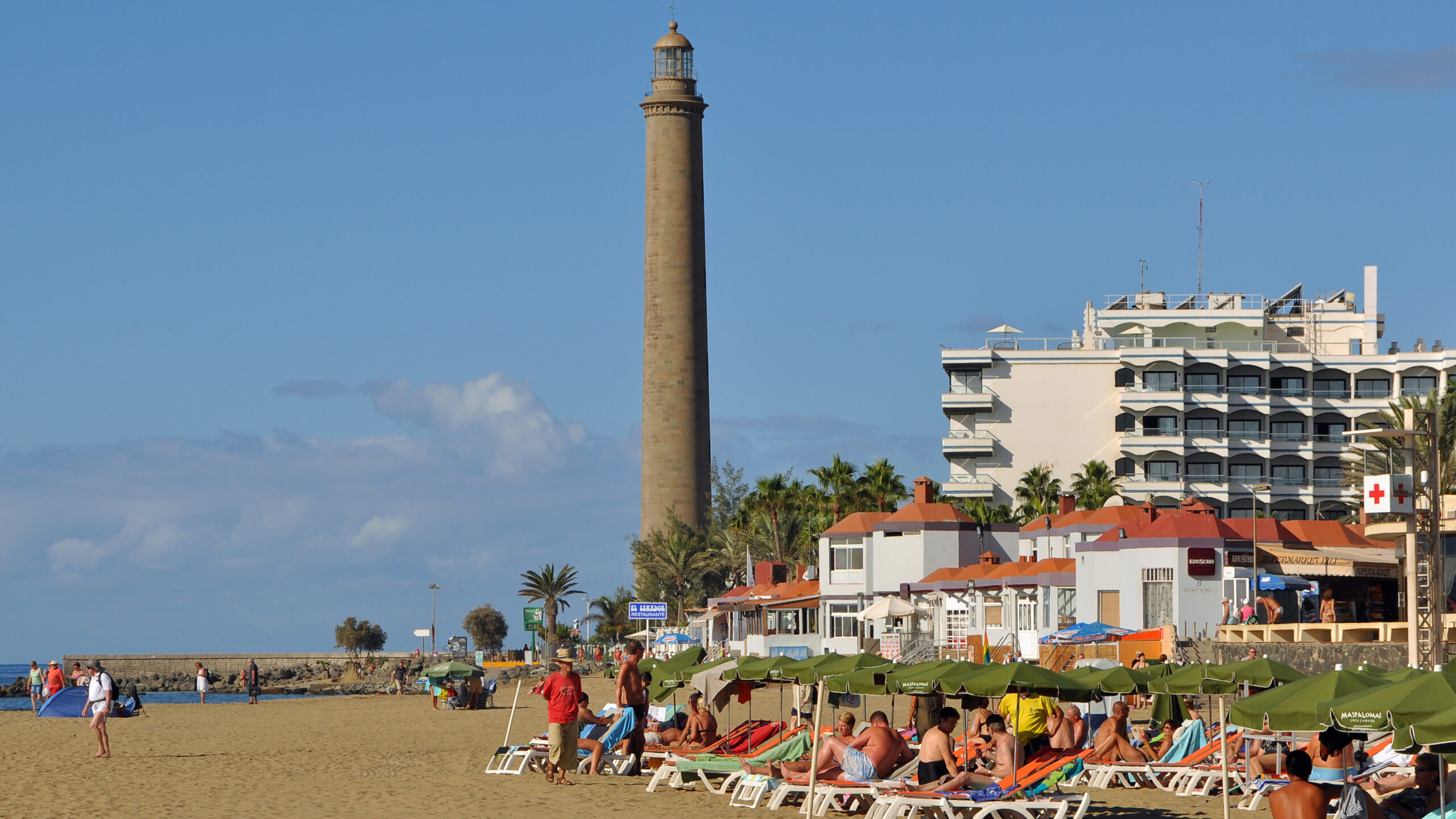 The Maspalomas Lighthouse dominates the beachfront, providing a historic landmark above the popular sandy shore.