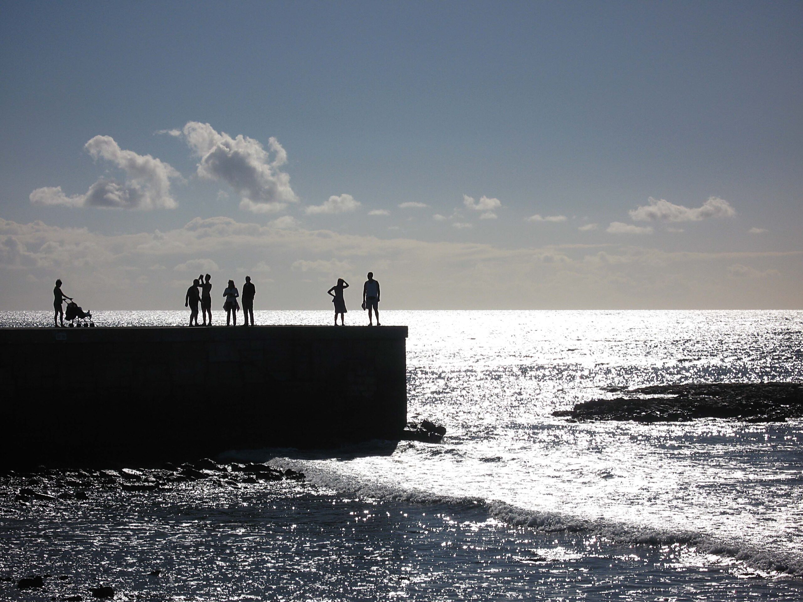 Visitors gather on the rocky shoreline near Maspalomas, enjoying views of the Atlantic coast.