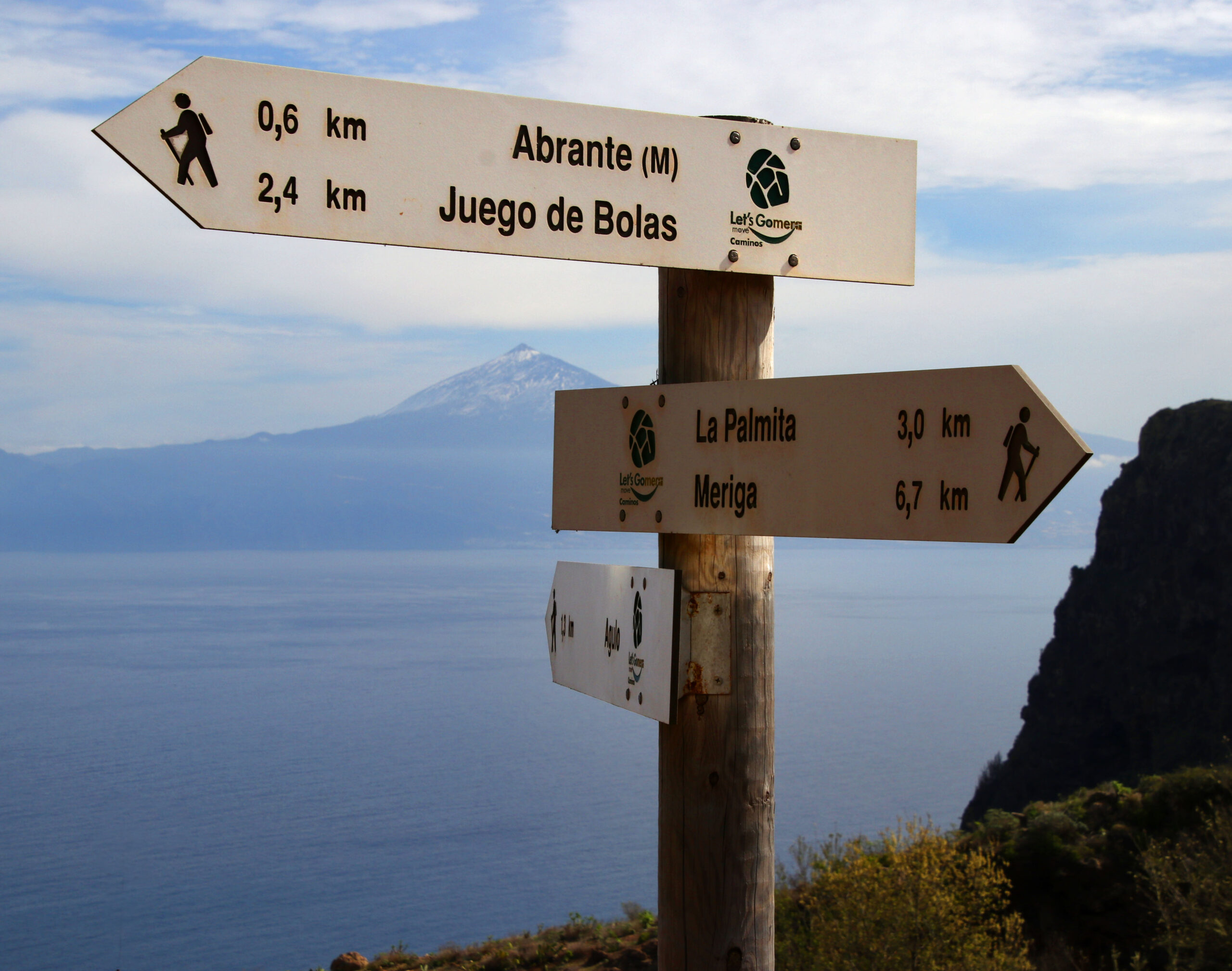 Directional hiking signs at Mirador de Abrante point toward nearby trails, with Tenerife's volcanic peak visible across the waters of the Canary Islands.